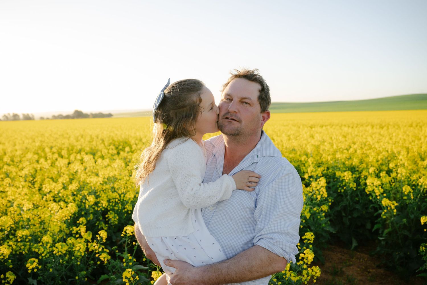 Couple embracing in a vibrant yellow canola field during golden hour.
