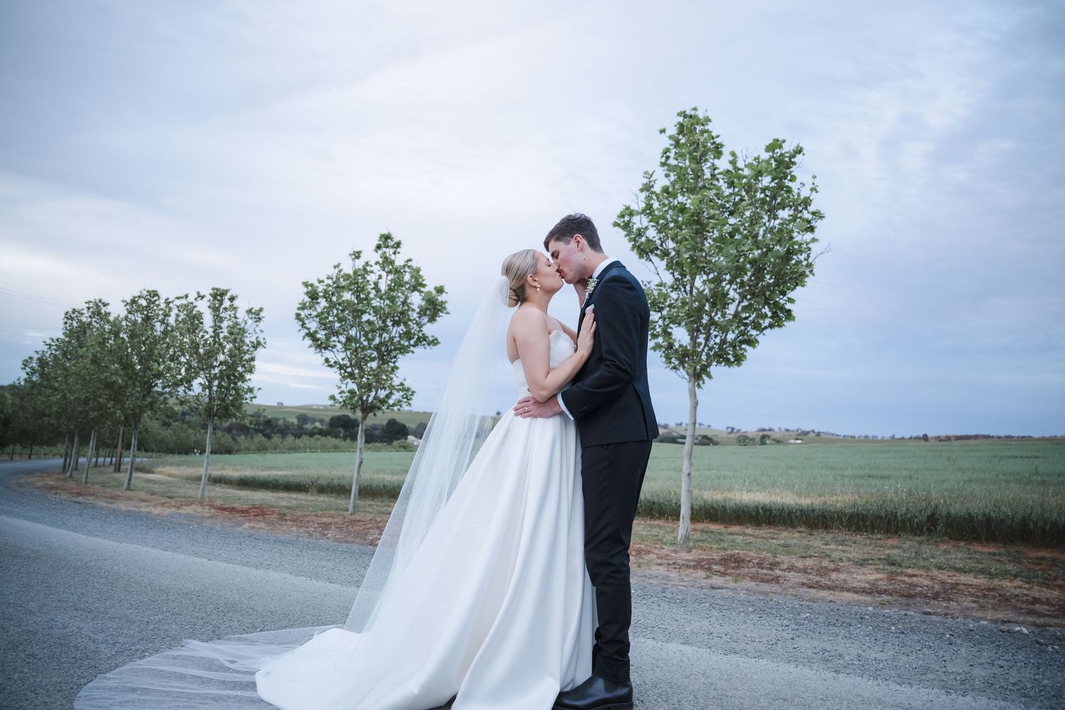 A couple in wedding attire embraces in front of a scenic rural landscape during their special day.