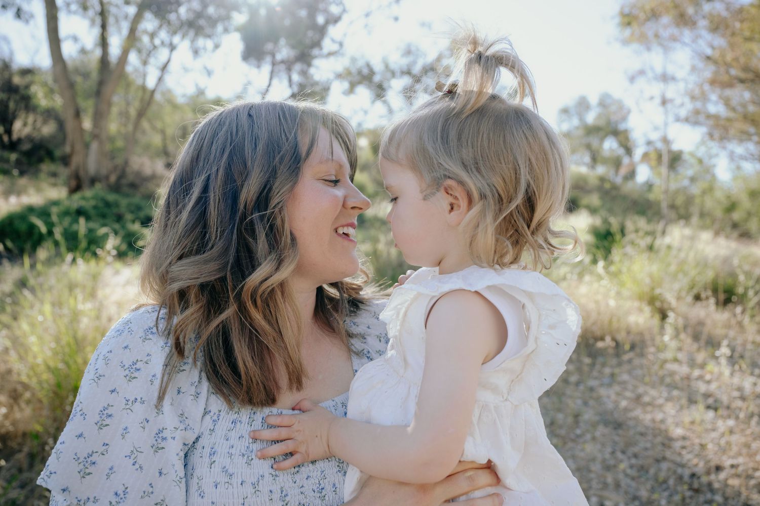A tender moment shared between two people wearing white dresses while standing in a sunlit outdoor setting.