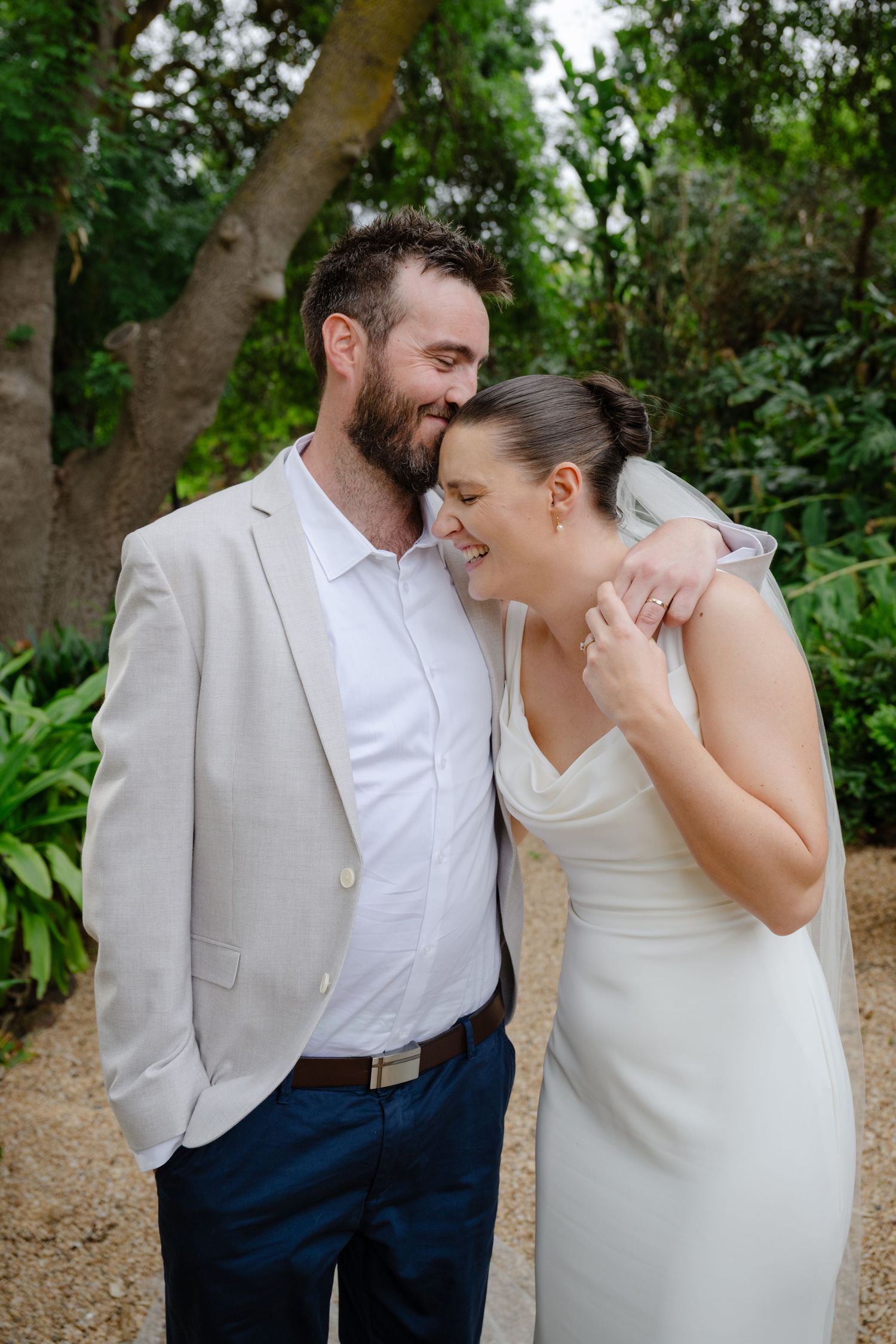 A couple shares a candid, joyful moment together in an outdoor garden setting wearing coordinated wedding attire.