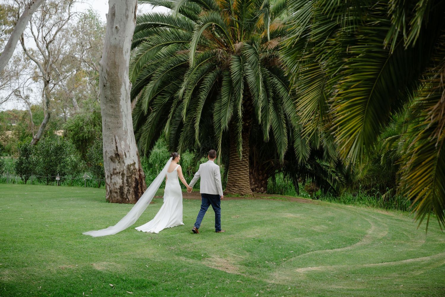 Couple walking through a lush green garden with palm trees and a flowing white wedding dress.