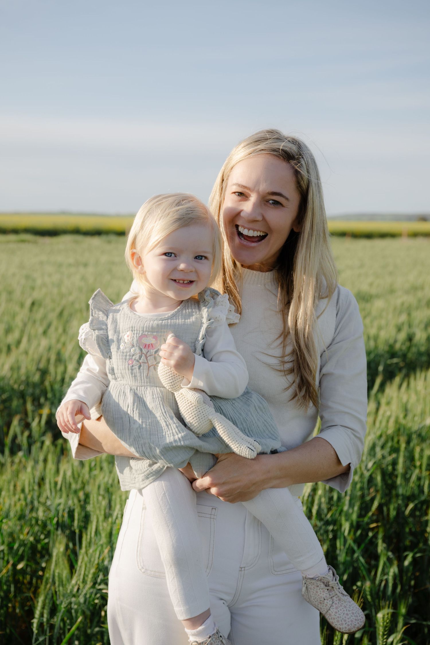 A parent and child share joyful moments together in a lush green wheat field on a sunny day.