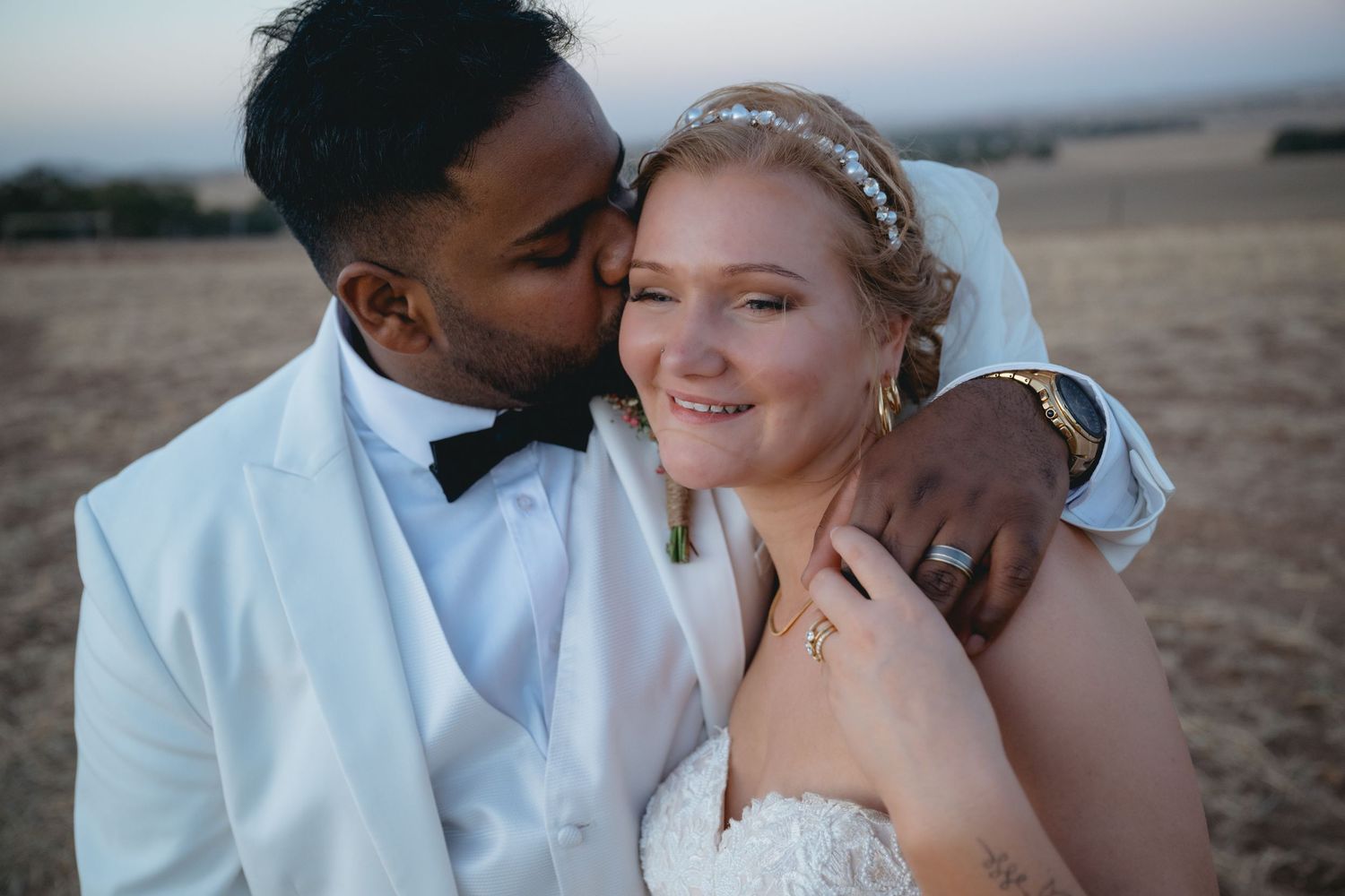 A romantic couple shares intimate moments together on a beach during sunset, dressed in white and casual attire.