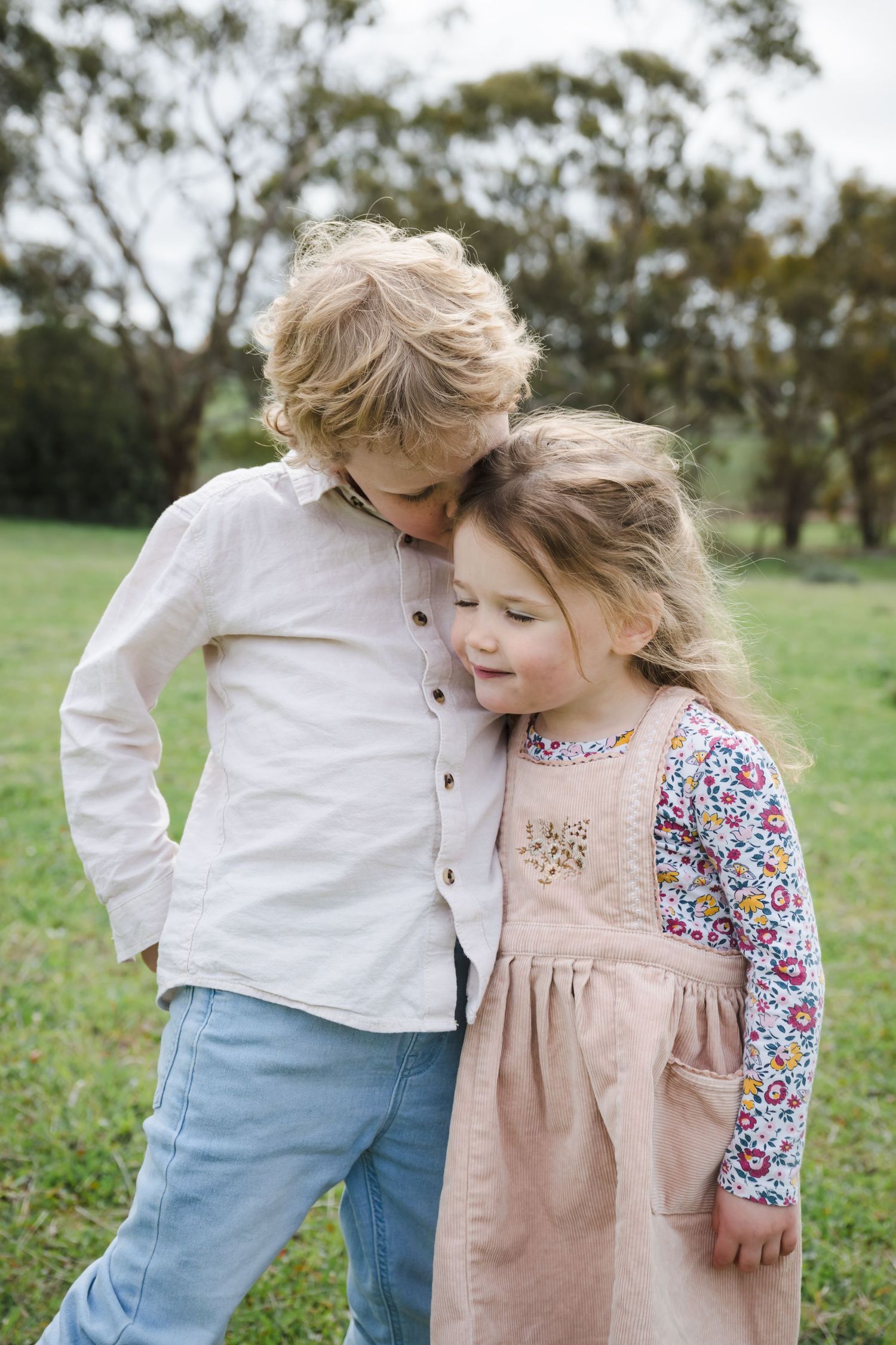 Sweet candid moment captured between two young siblings playing together in a grassy field on a sunny day.