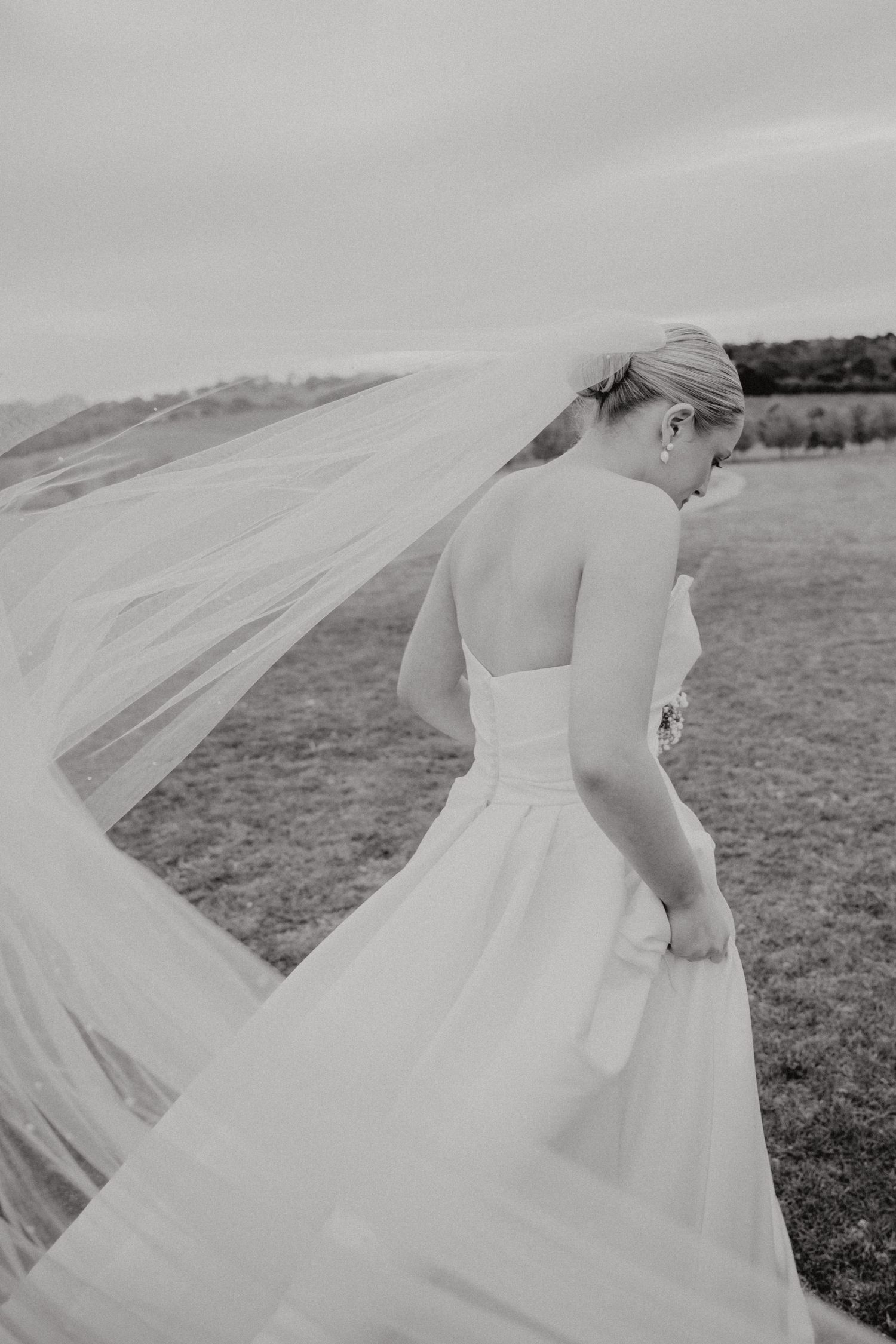 A flowing white wedding veil billows dramatically in the wind across a cloudy outdoor setting.