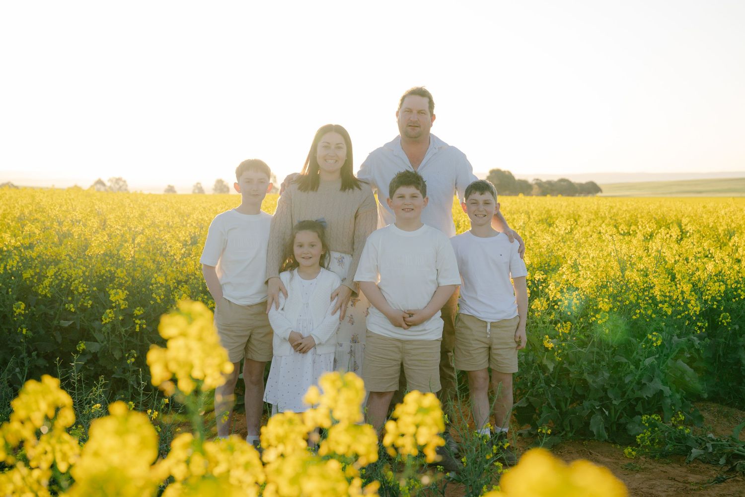 Family enjoying a sunset walk through a vibrant yellow canola field on a warm summer evening.