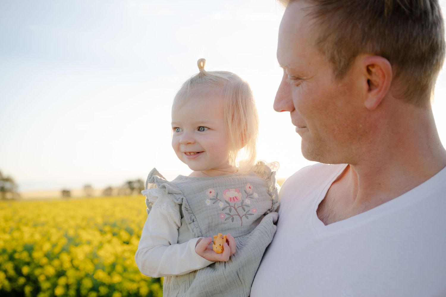 Family enjoying a tender moment together in a sunlit field of yellow wildflowers at sunset.