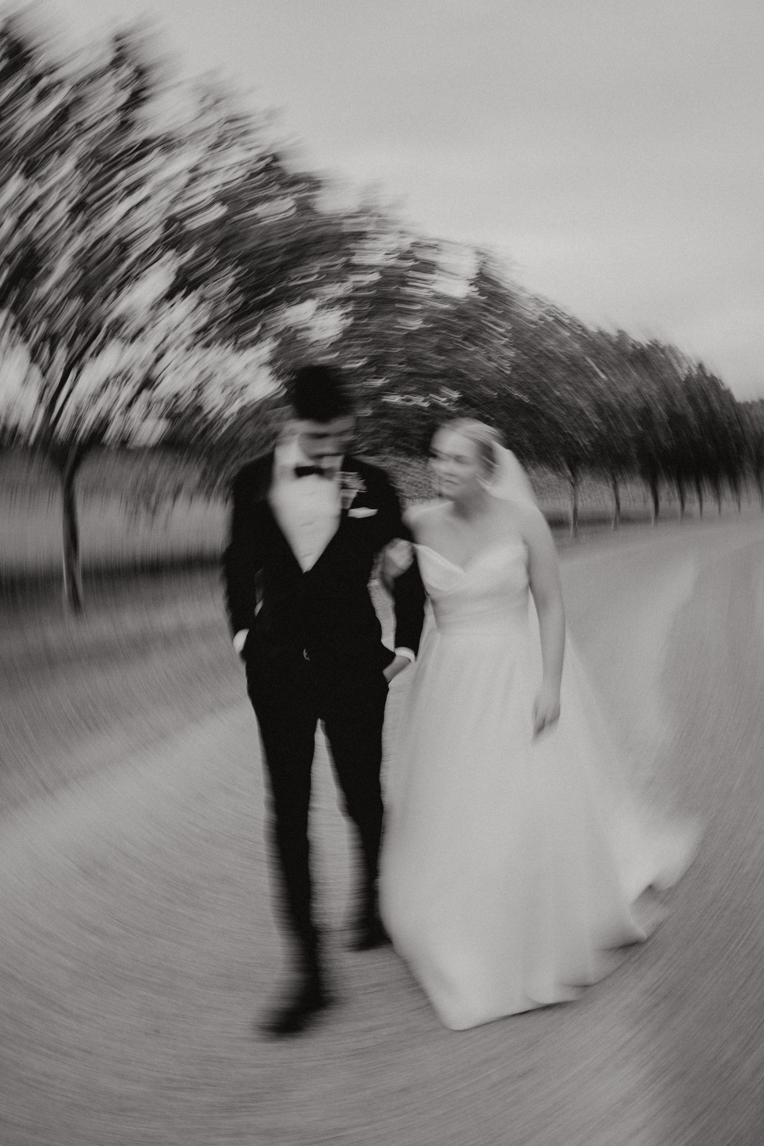 A black and white motion blur photo sequence shows a couple walking along a tree-lined path in wedding attire.