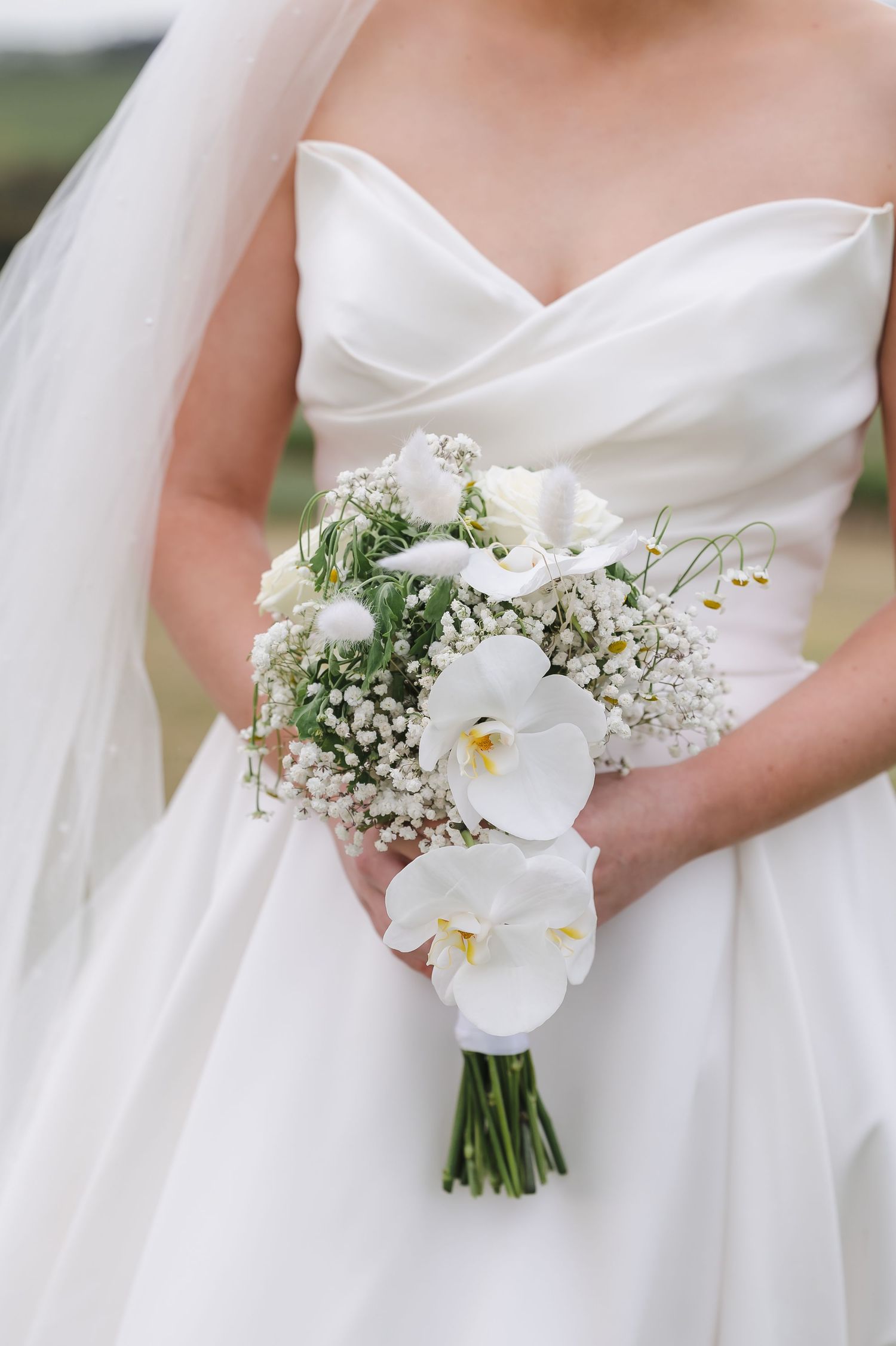 A white bridal bouquet featuring orchids and baby's breath against a flowing white wedding dress.
