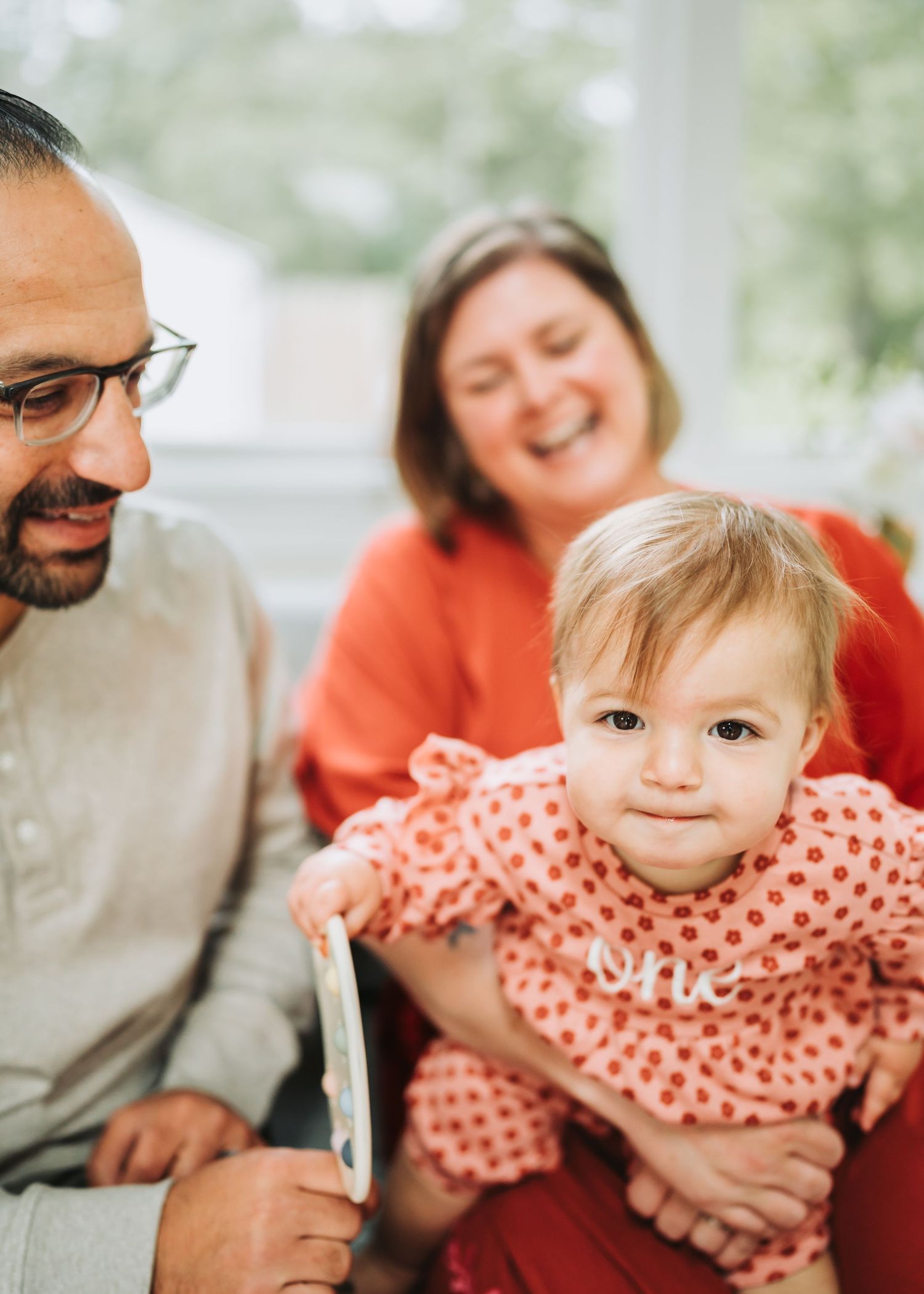 A happy family moment captured as they smile and play with a baby in a coral polka dot outfit.