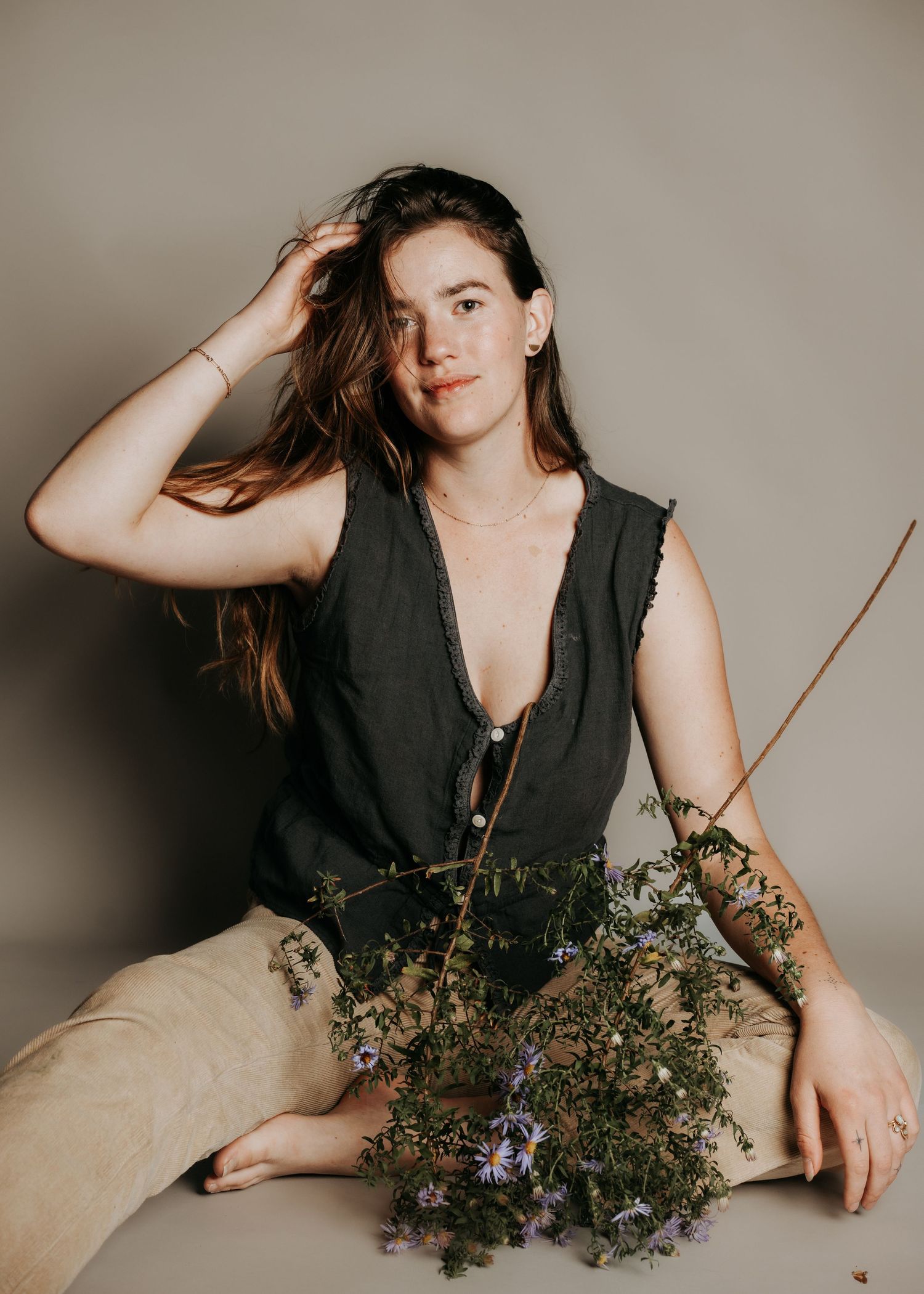 Artistic portrait with dried flowers and black sleeveless top against neutral background.
