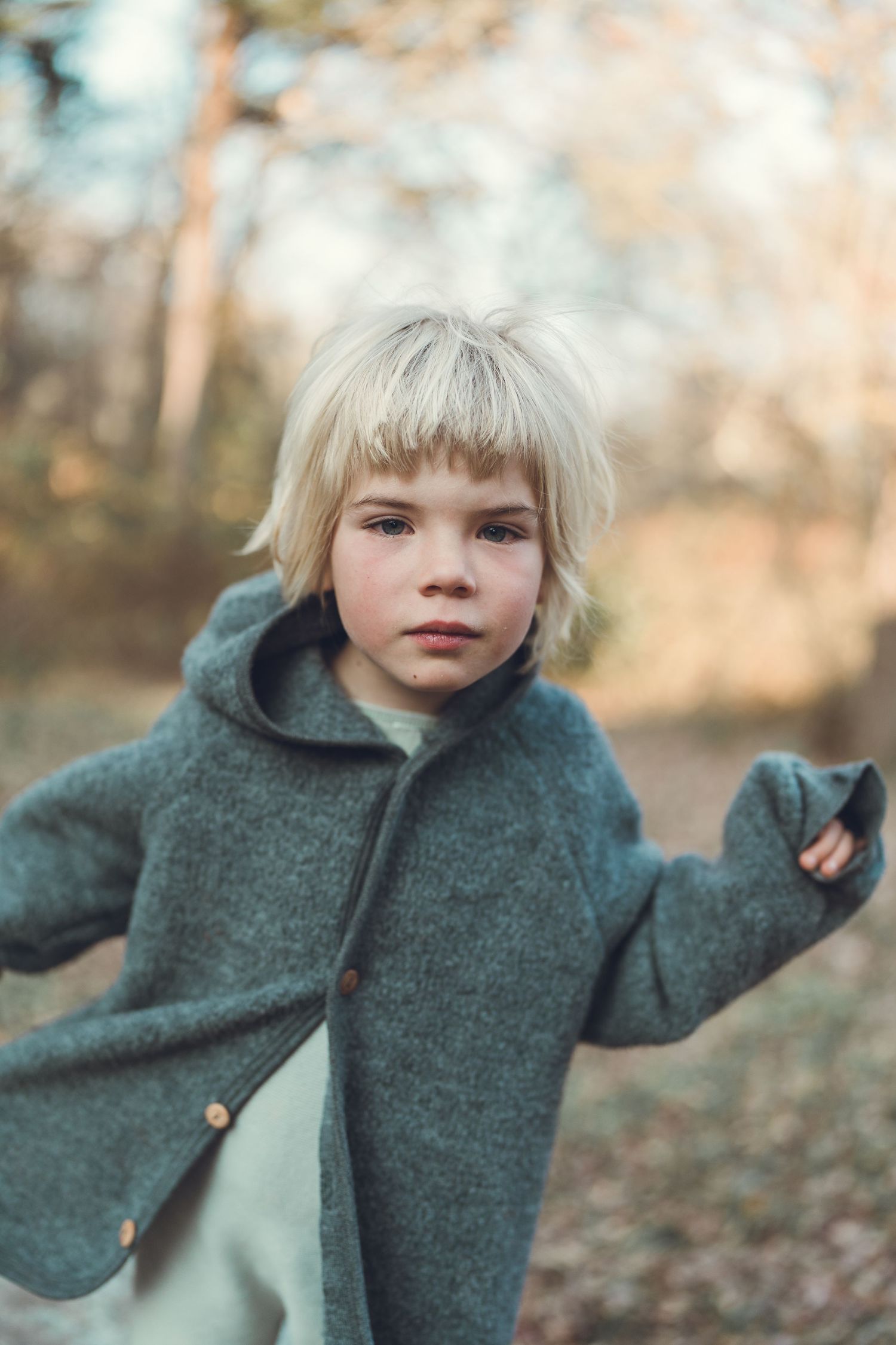 Child in a green wool coat standing in an autumn forest setting.