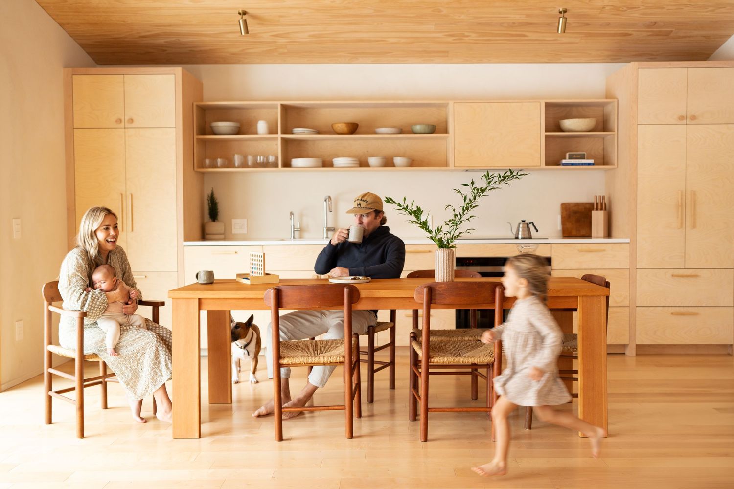 Modern wooden kitchen with family gathering around dining table in warm lighting.