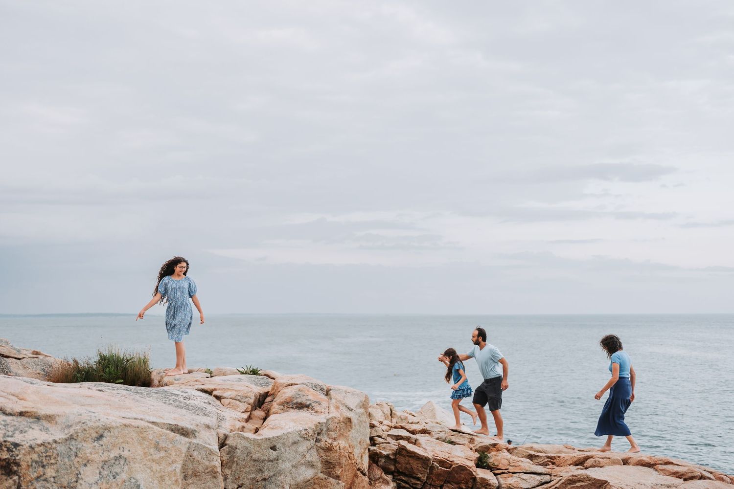 Group walking along rugged coastal rocks with ocean views under an overcast sky.
