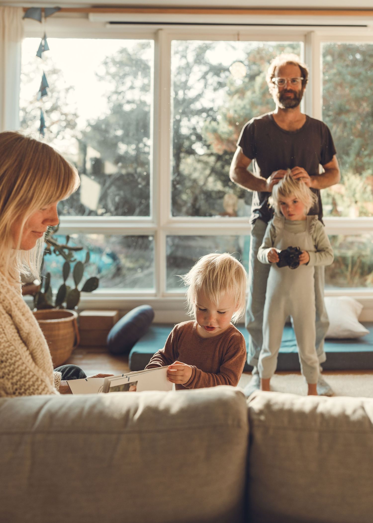 Cozy family scene in sunlit living room with large windows and comfortable furniture.