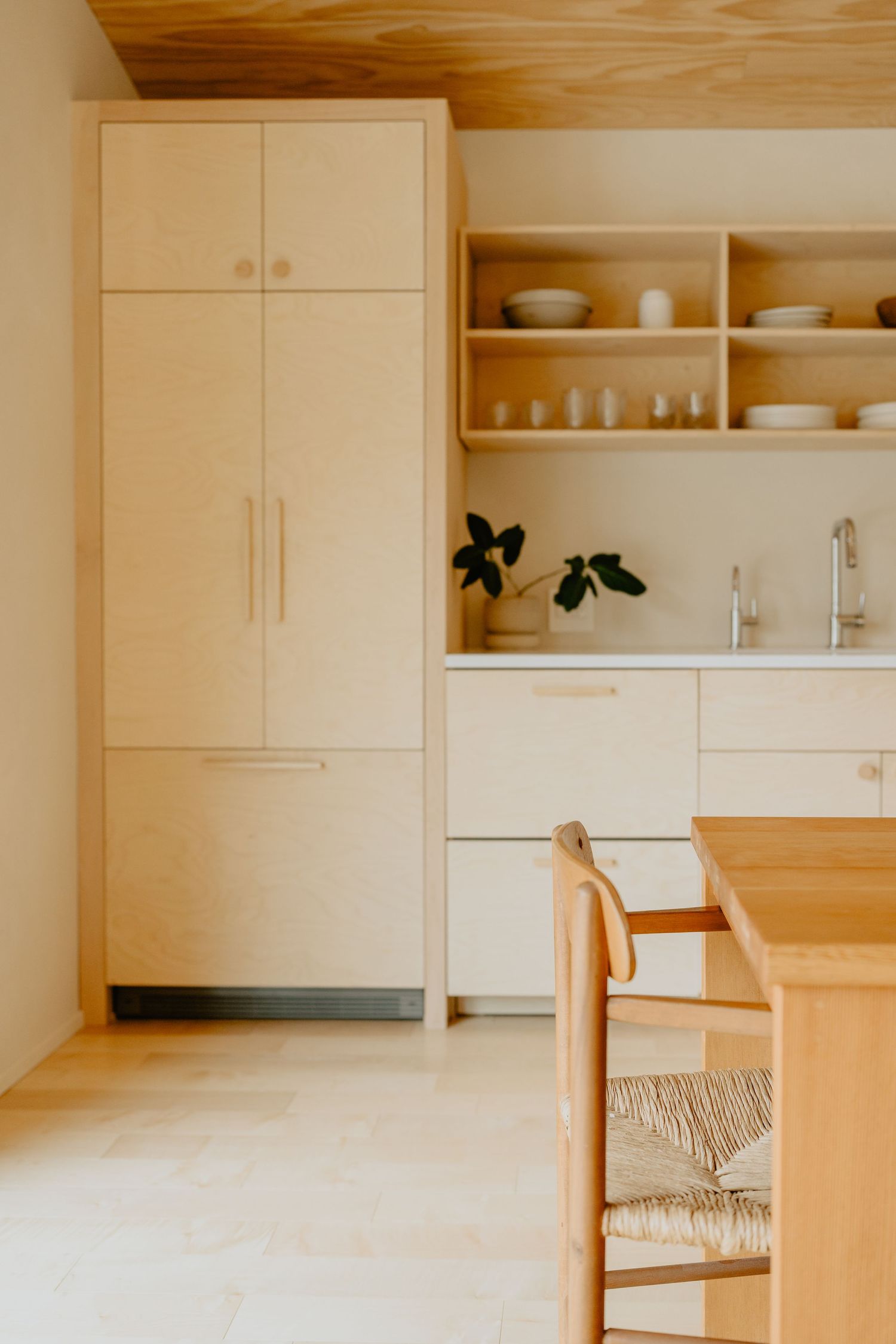 Modern minimalist kitchen with white cabinets, wooden chair, and open shelving.