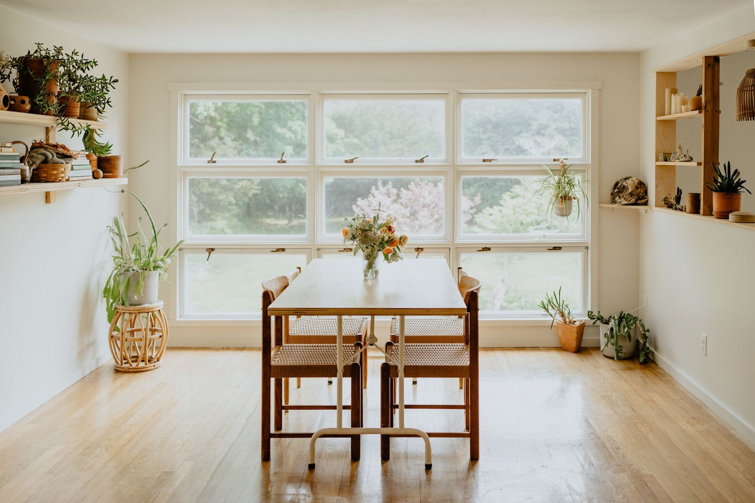 Bright and airy open concept living space with wooden furniture and hanging plants near large windows.