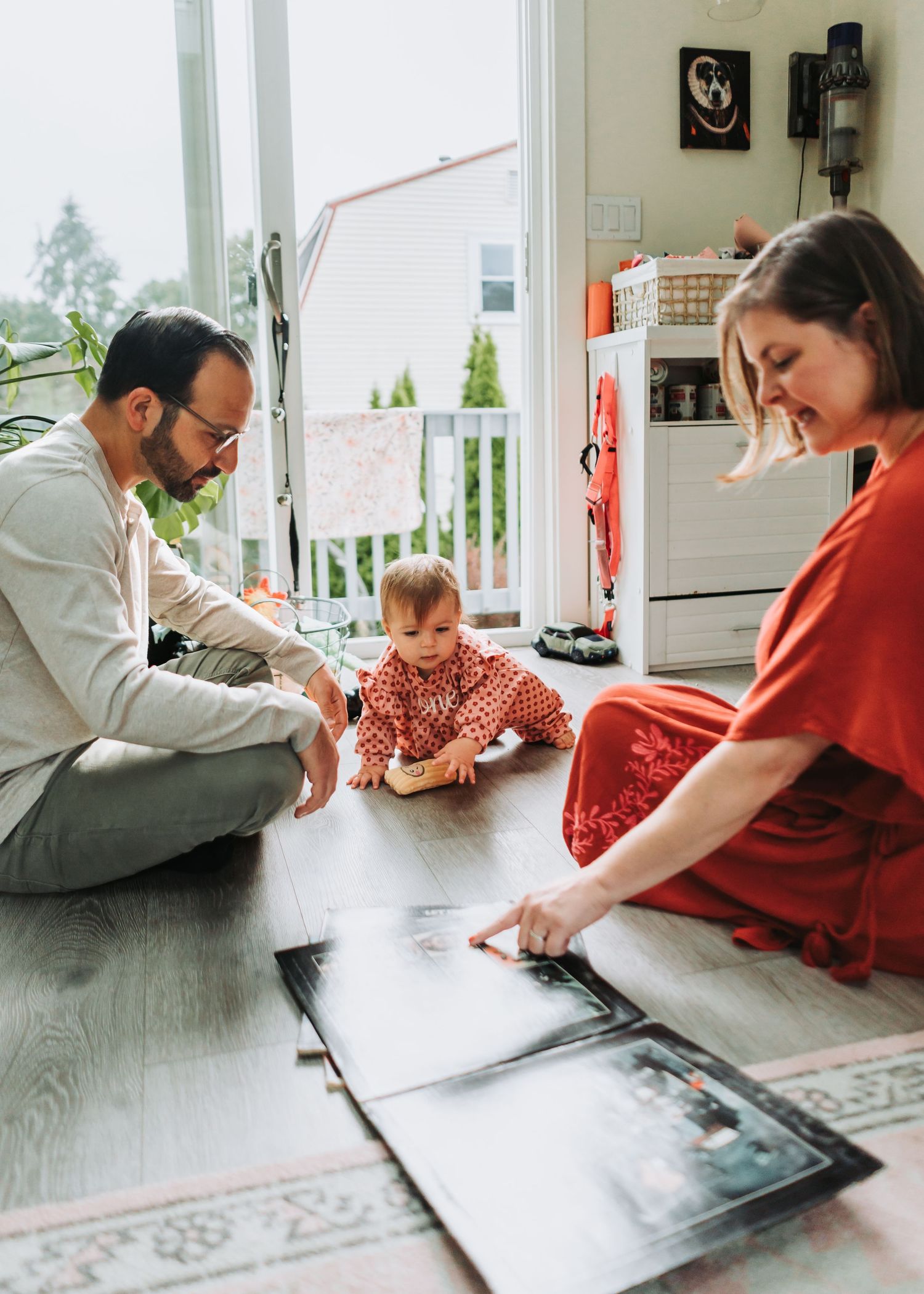 A parent and child lie on a wooden floor together looking at a tablet device during a casual indoor moment.