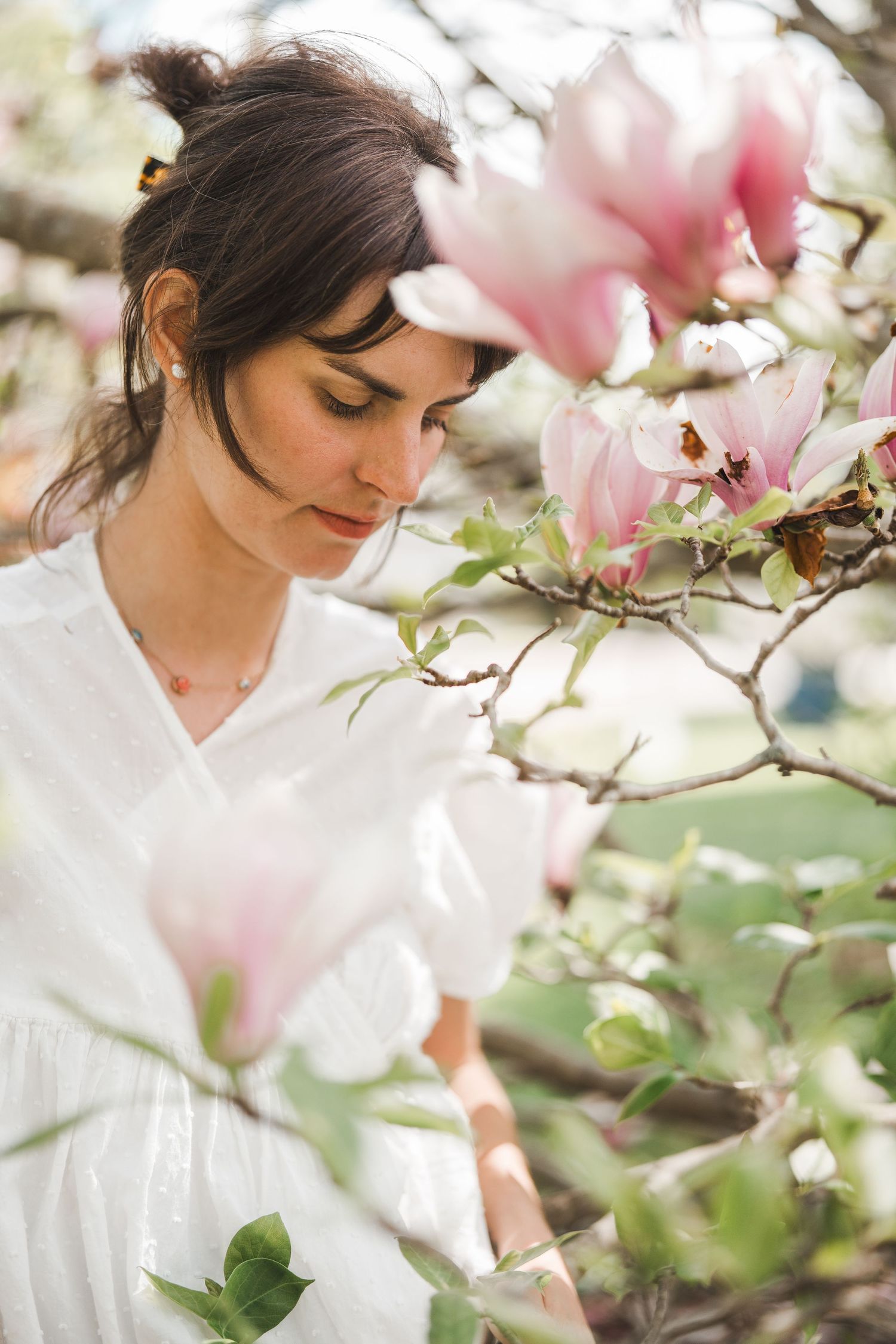 A dreamy spring portrait among blooming pink magnolia flowers in a garden setting.