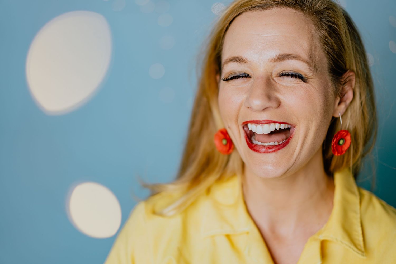 A joyful expression captured against a yellow and blue background with red earrings.
