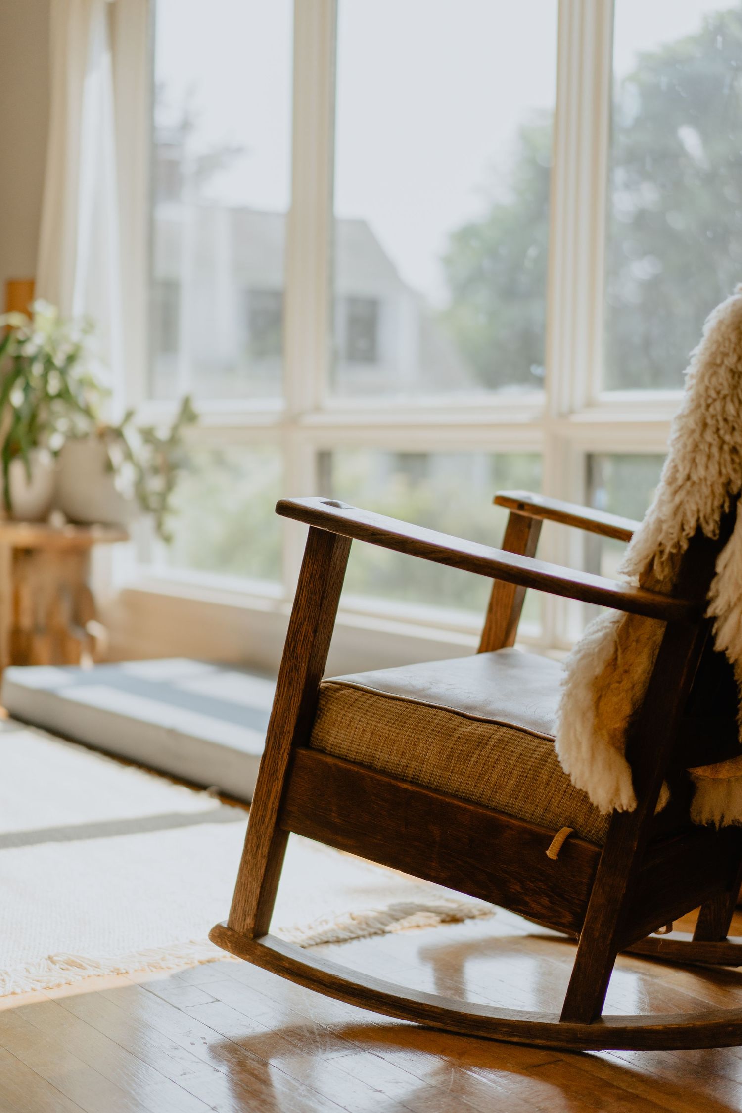 Wooden rocking chair with cushions by large windows overlooking a misty outdoor view.
