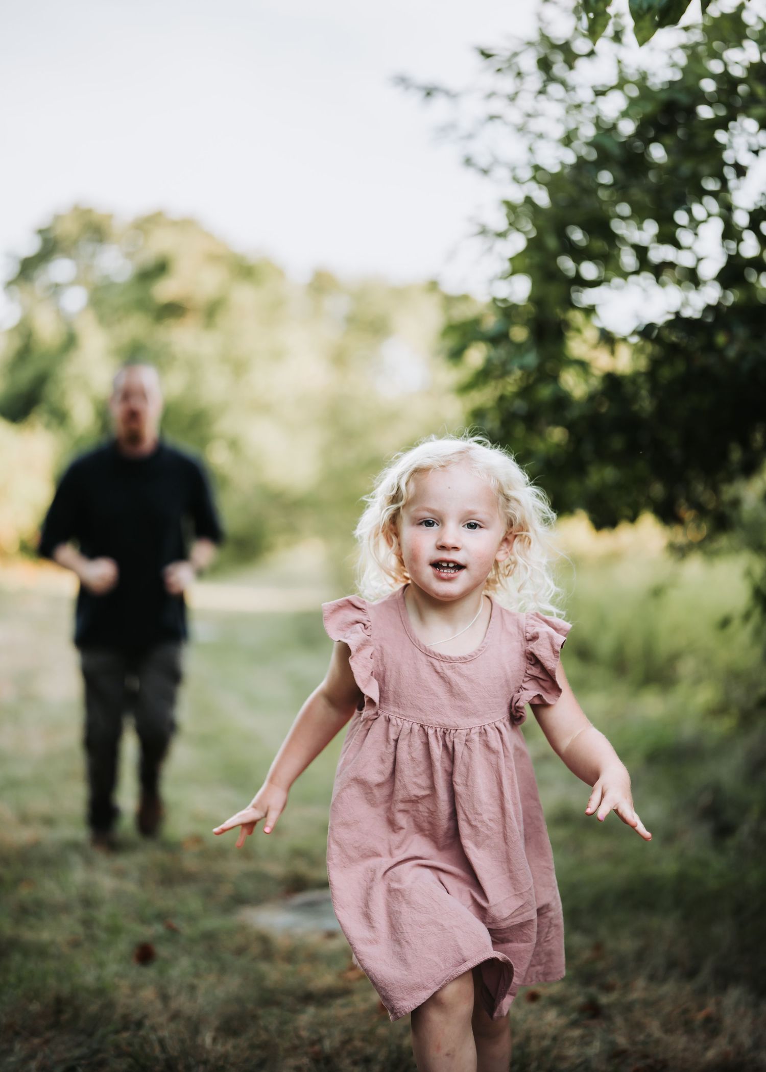 Small child in pink dress runs playfully through a grassy outdoor setting at sunset.