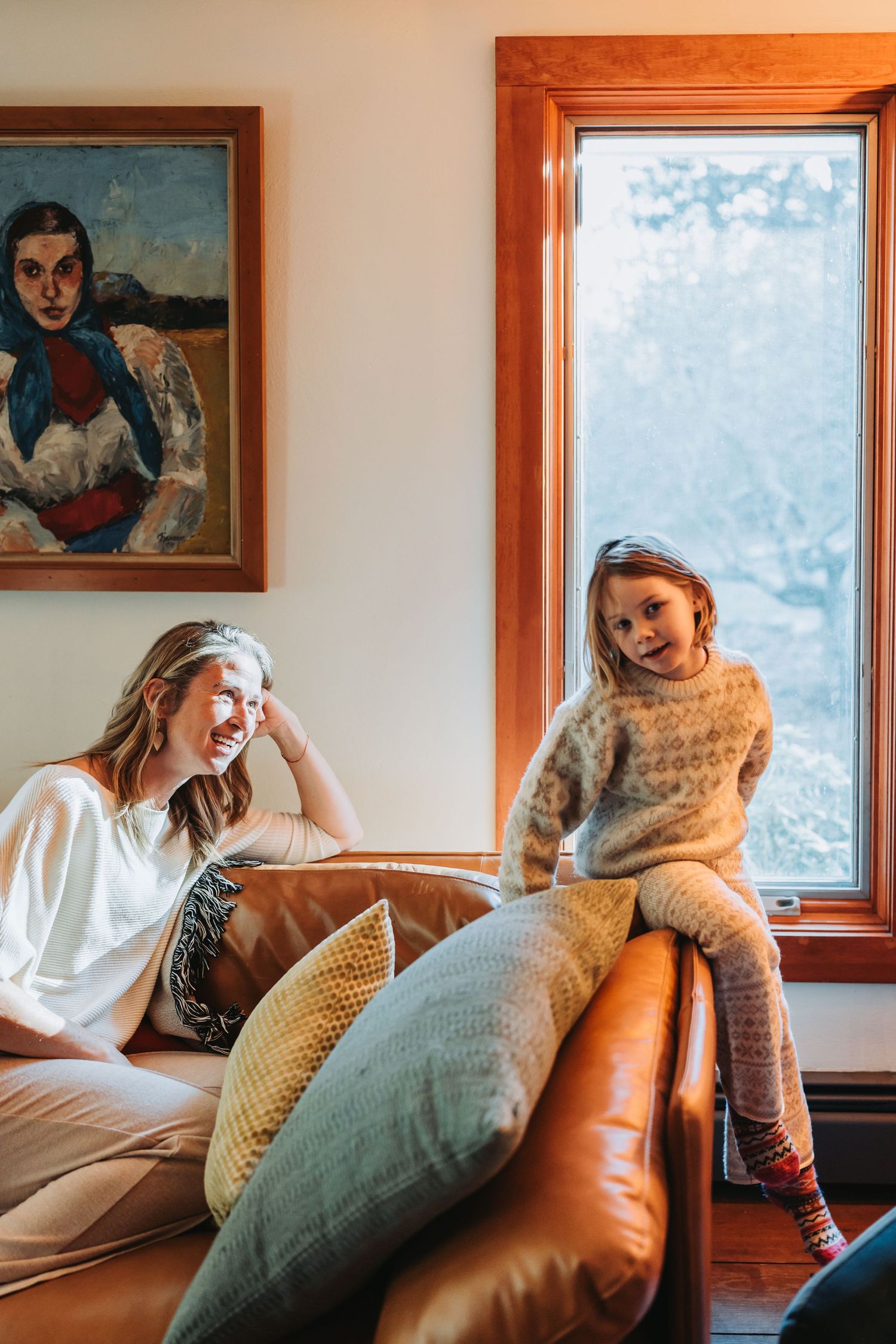 A series of connected photos showing someone lounging on a brown leather couch near a window with artwork on the wall.