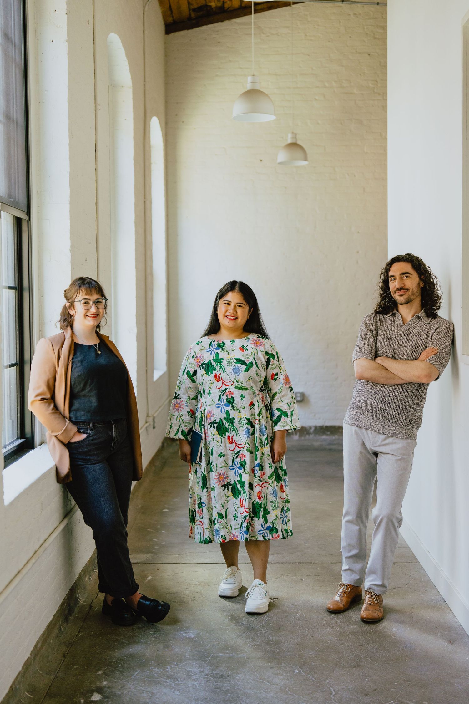 Three people standing in a bright hallway with white walls and pendant lighting.