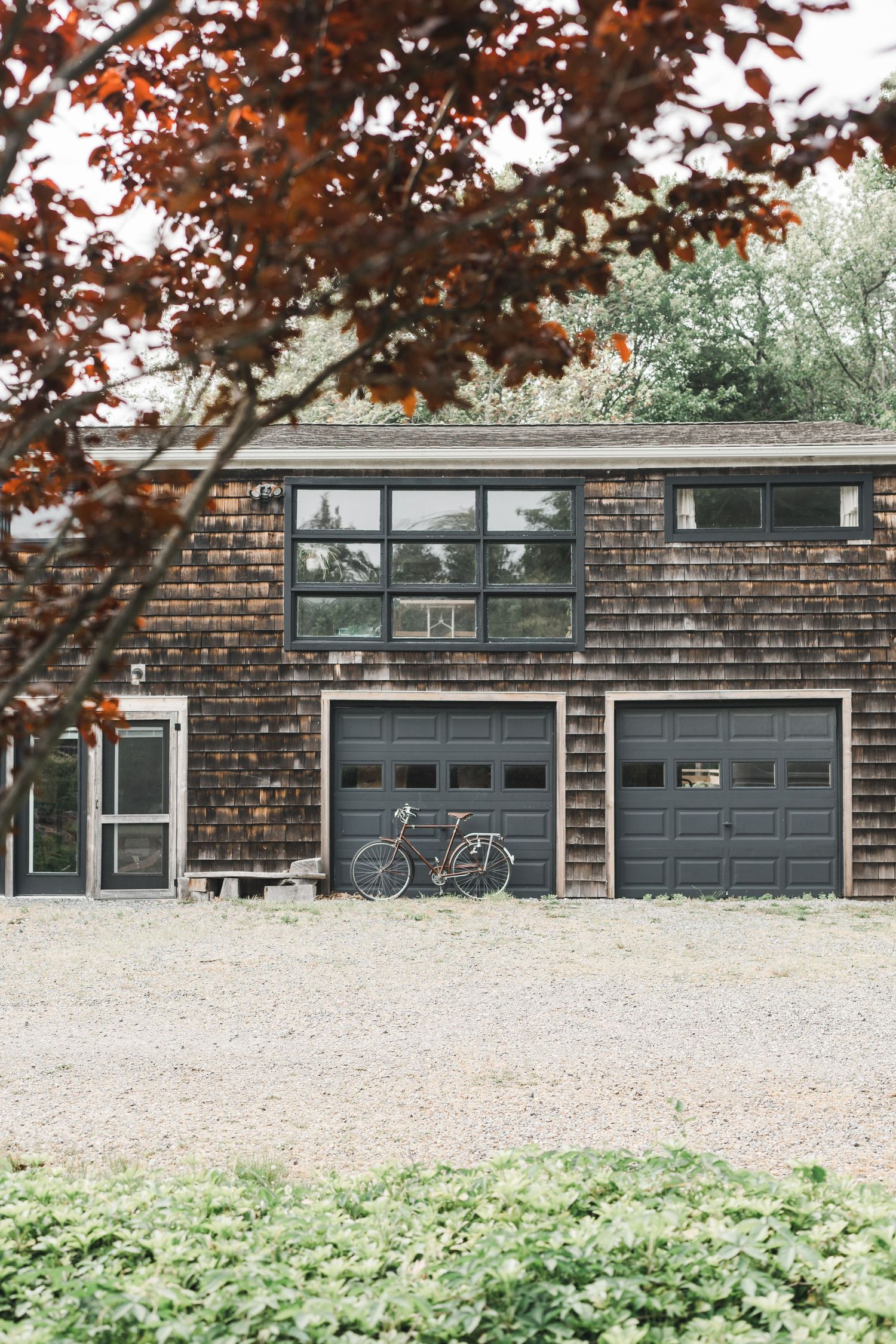 Minimalist brown brick building with a modern dark garage door and green foliage in the foreground.