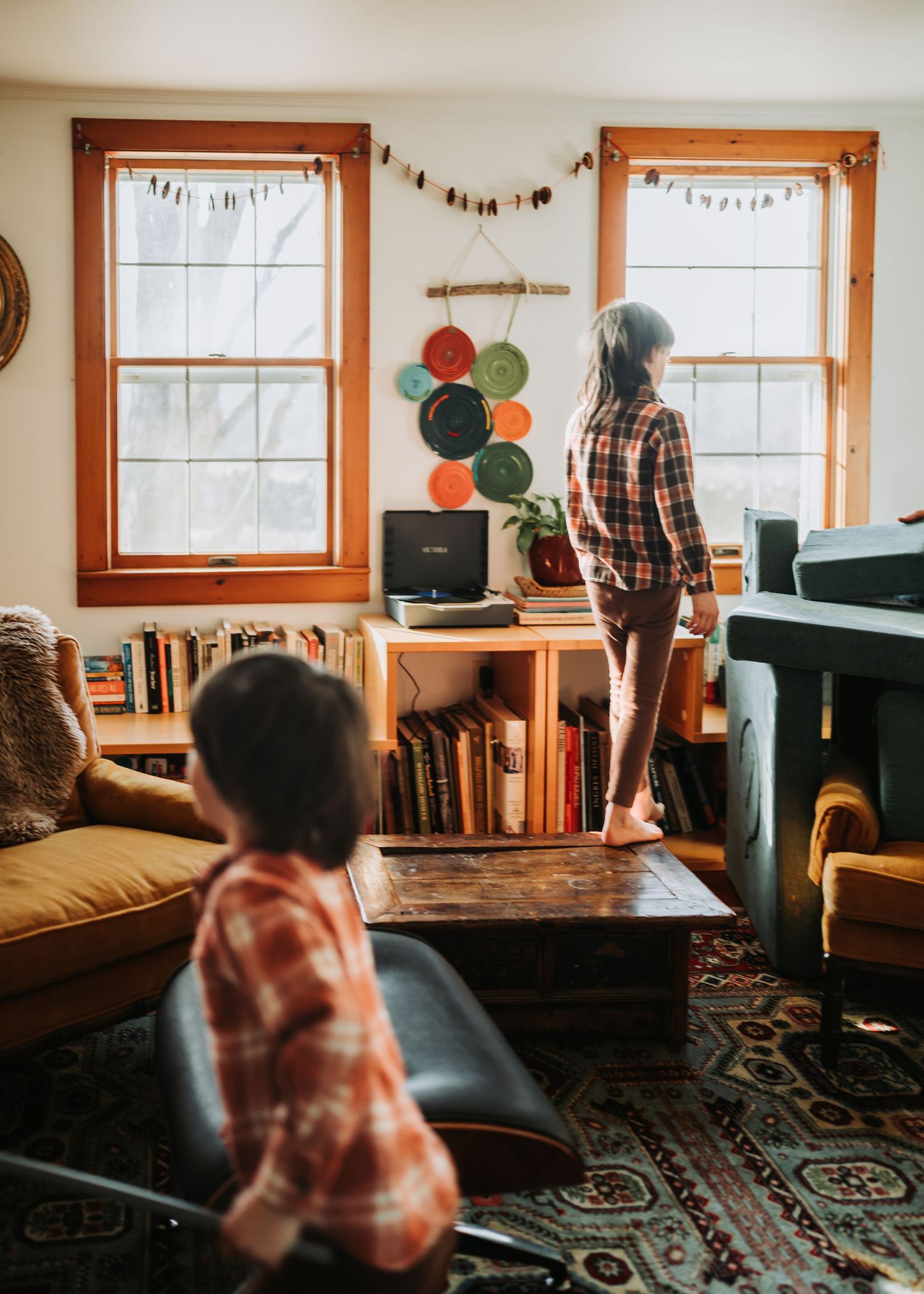 A cozy living room with wooden window frames, bookshelves, and a decorative patterned rug showing different angles.