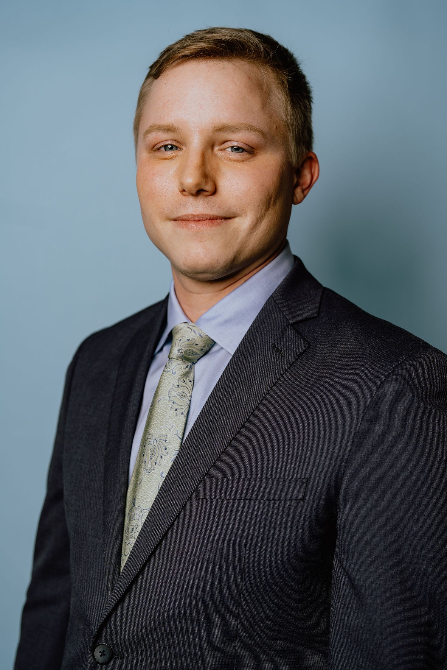 Professional headshot series showing different angles of someone wearing a dark suit and patterned tie against a blue backdrop.