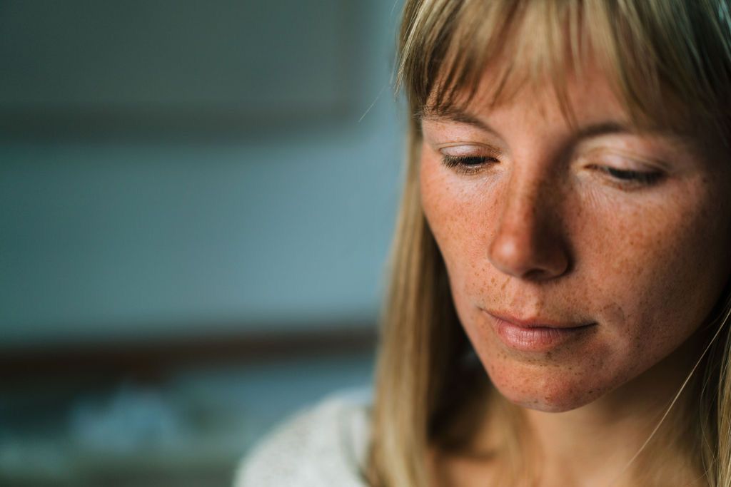 Close up portrait showing freckles and downward gaze against teal background in soft lighting.