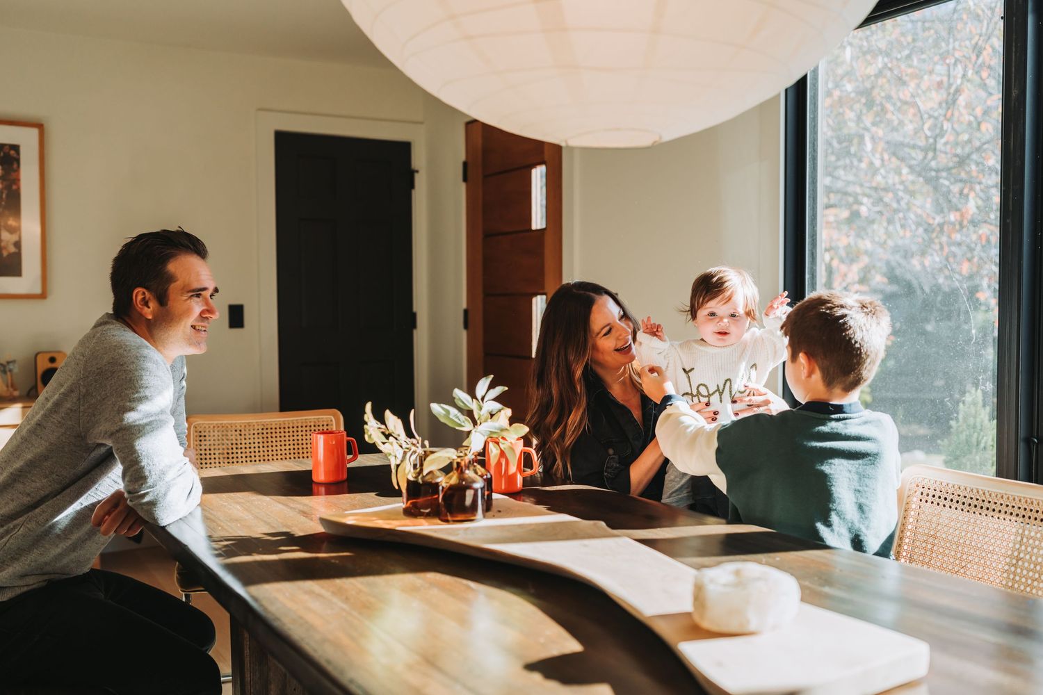 Candid family moment around dining table with paper lantern light fixture overhead.