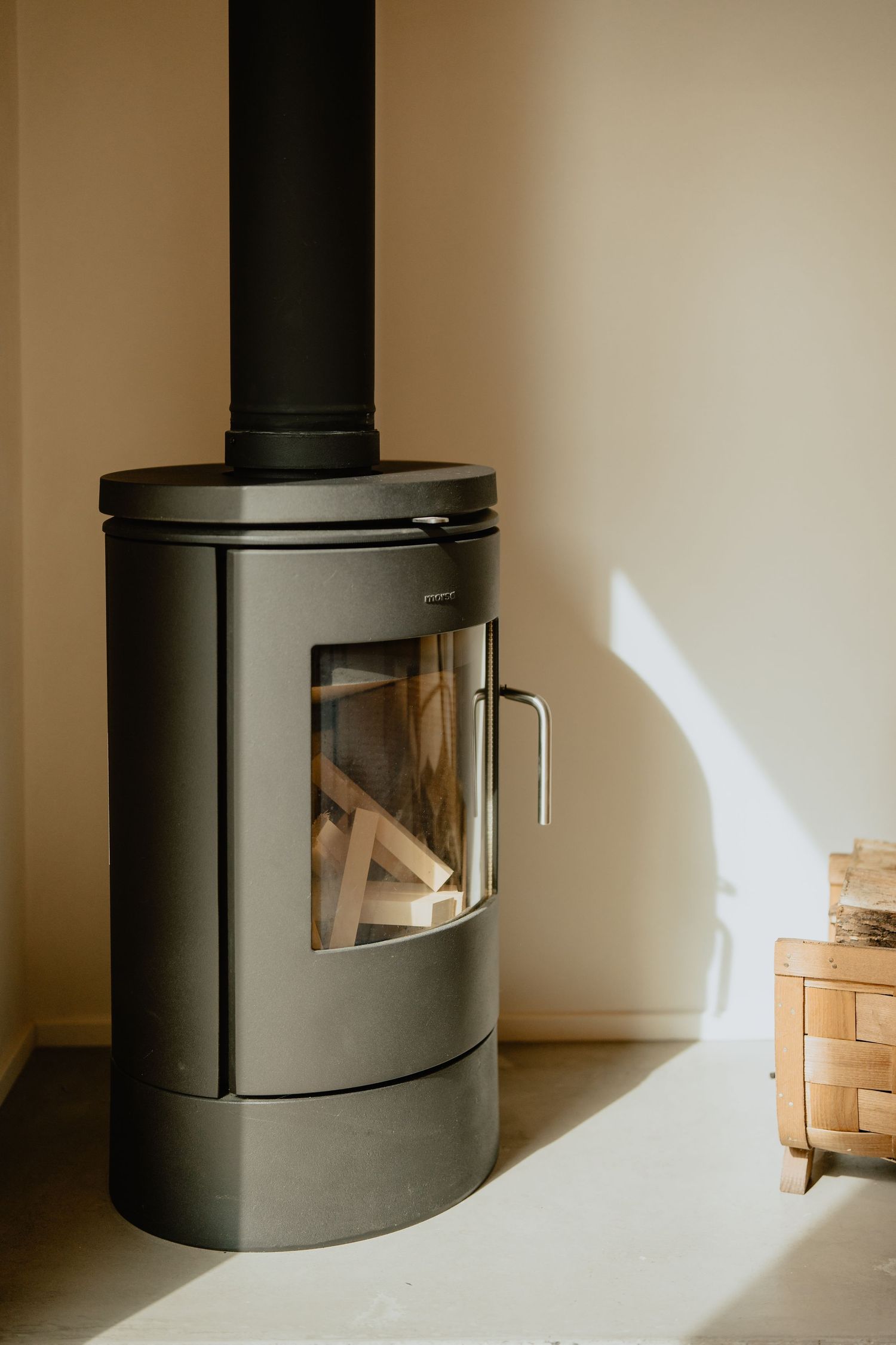 Modern wood-burning stove with glass door and stacked firewood.