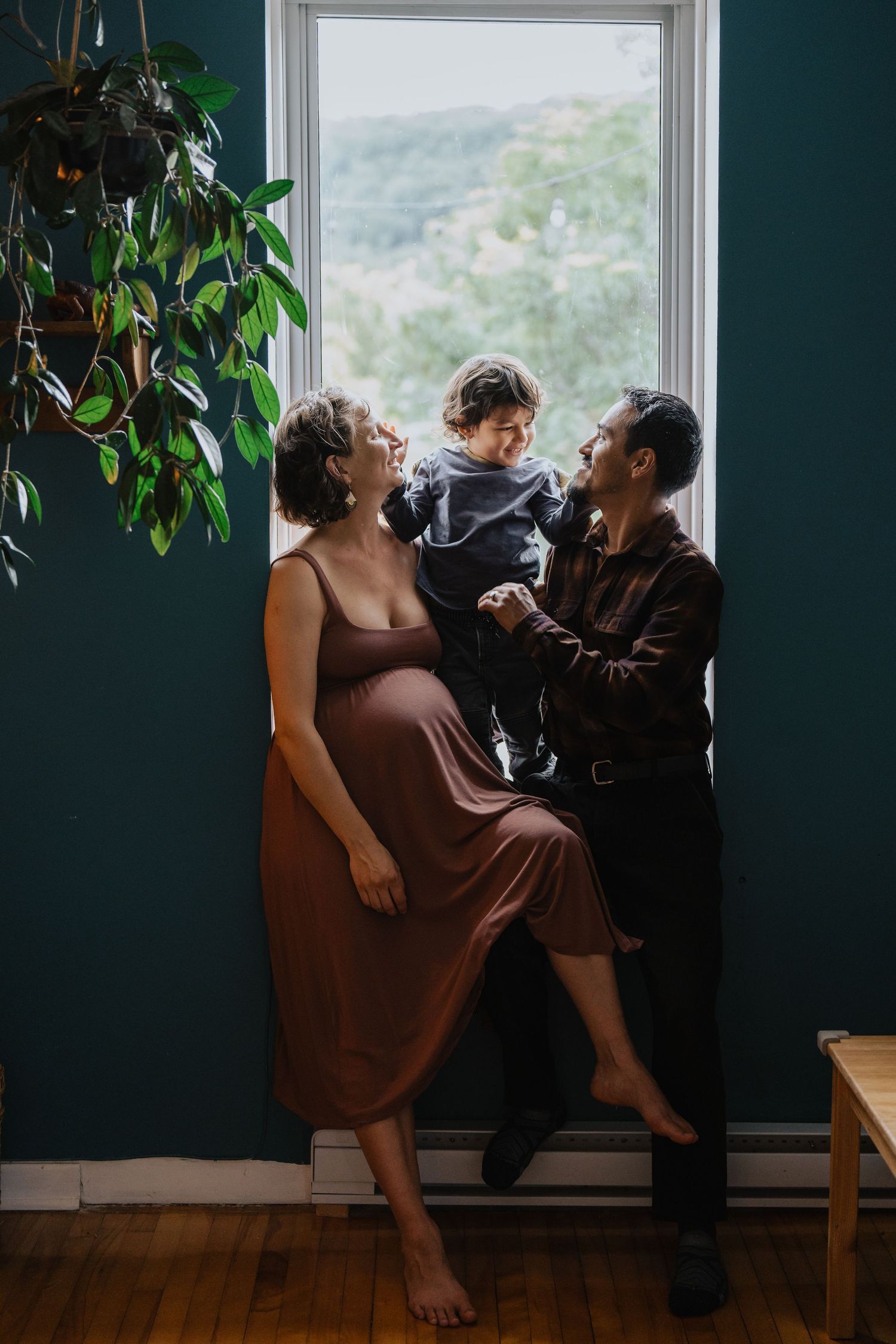 Intimate family moment by window with house plants and teal walls.
