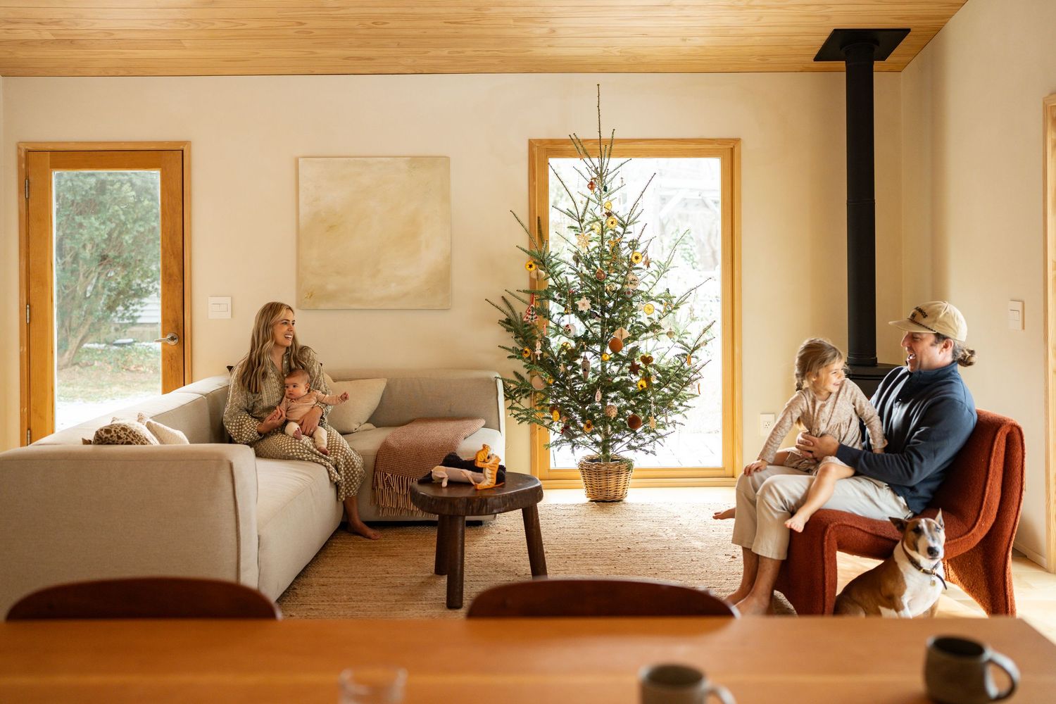 A cozy living room decorated for Christmas with a lit tree, modern furniture and large windows.