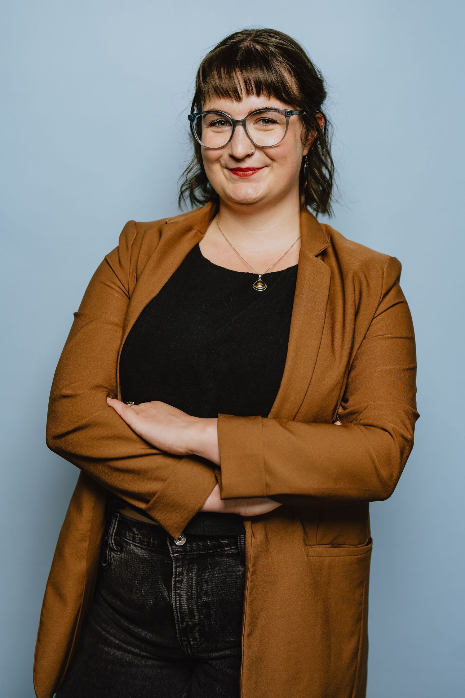 Professional portrait of person in brown blazer and black top against blue background.