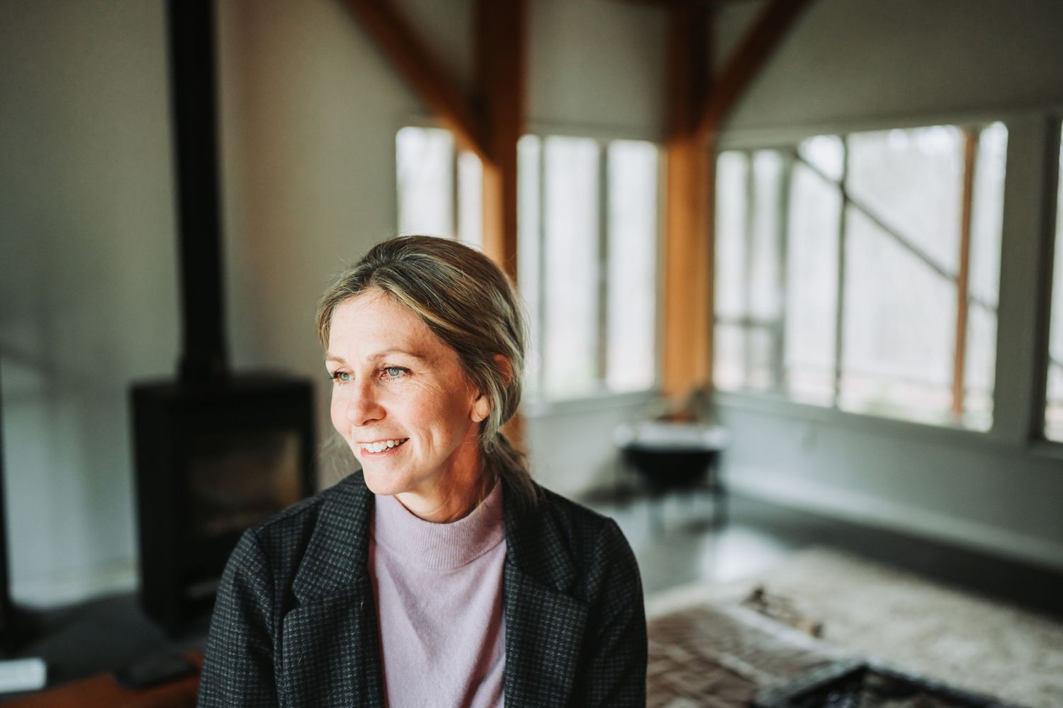 Someone wearing a light pink sweater gazes thoughtfully out a window in a naturally lit room.