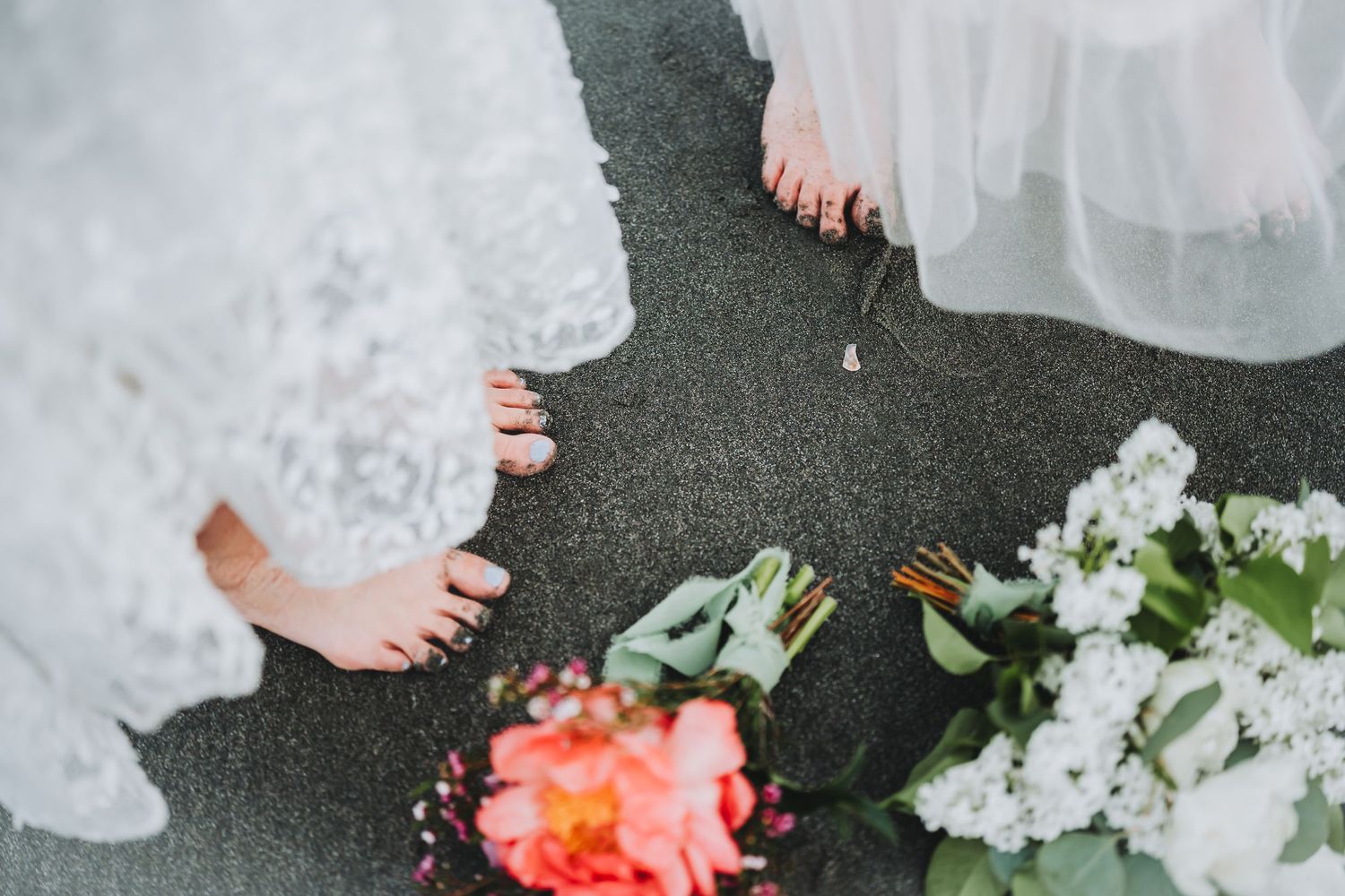 Close-up of white wedding dress details and coral pink flowers against dark background.