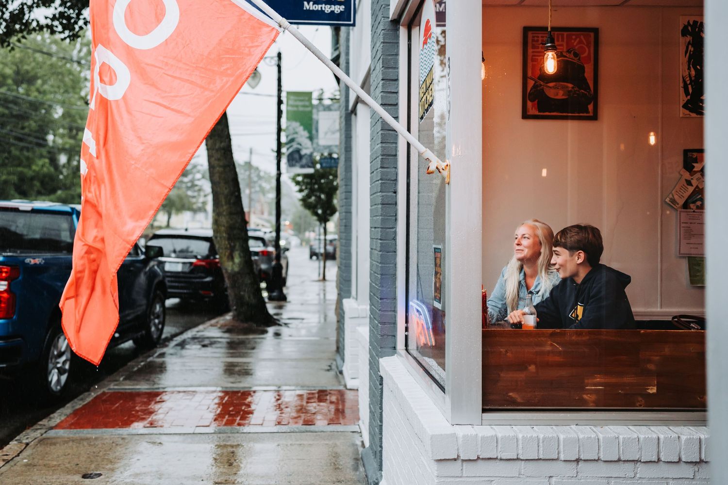 A series of five connected images showing bright orange flags waving in front of a storefront on a rainy day.