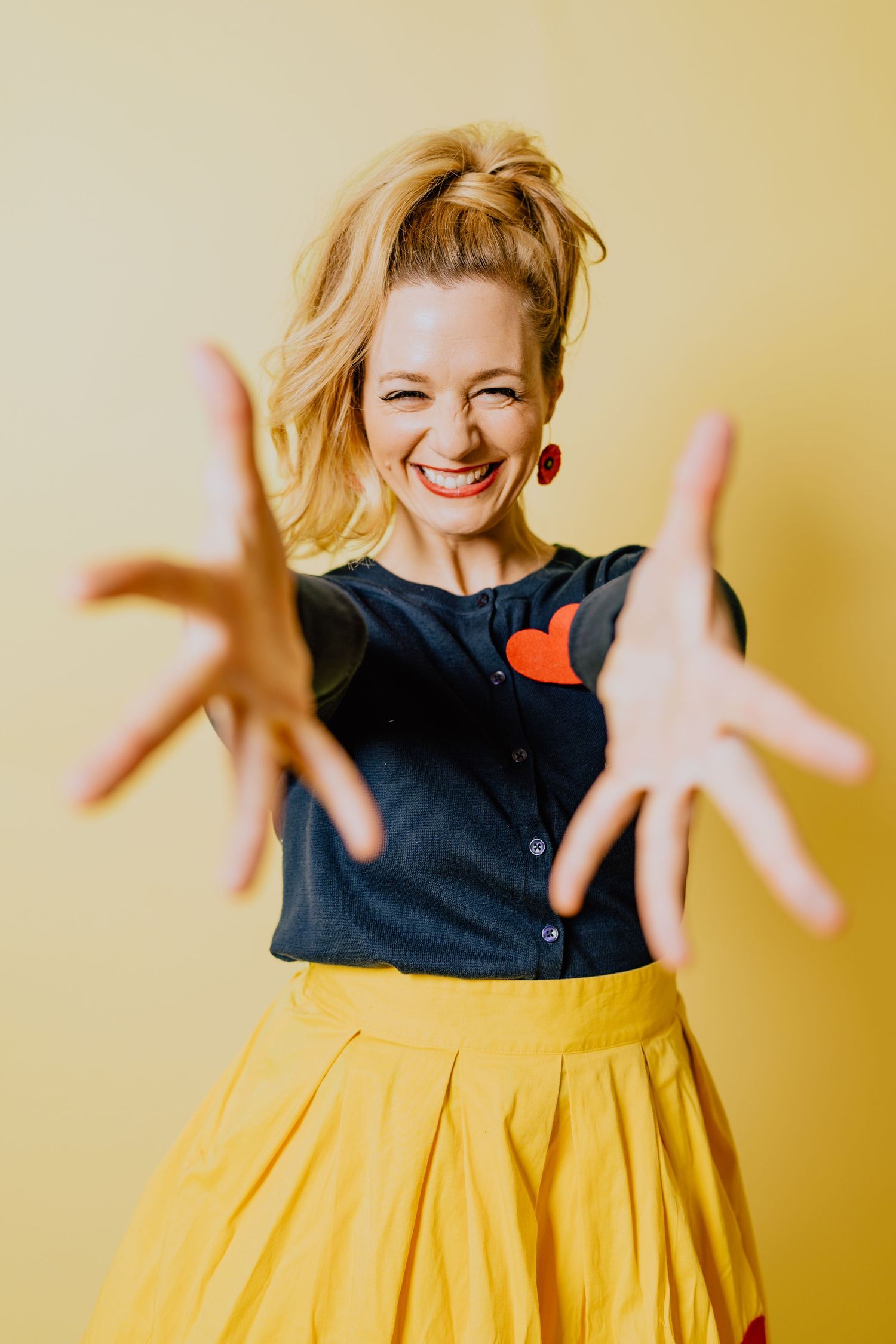 Joyful expression with hands reaching toward camera against yellow background.
