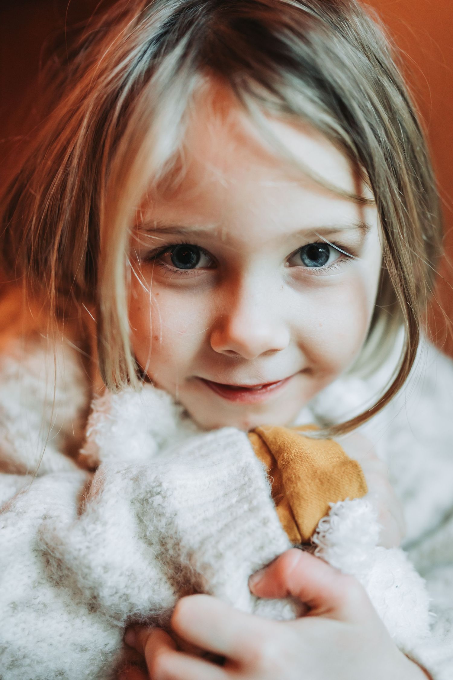 Close up portrait of child in white sweater with warm lighting and soft expression.