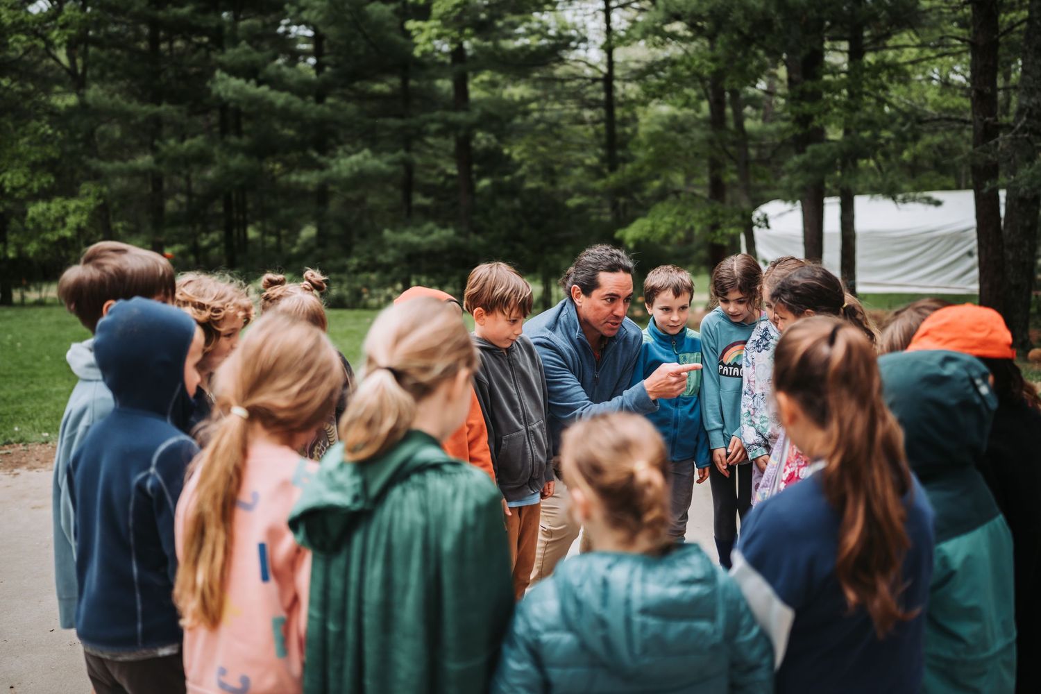 A group of people stand in a line outdoors surrounded by green trees and nature.