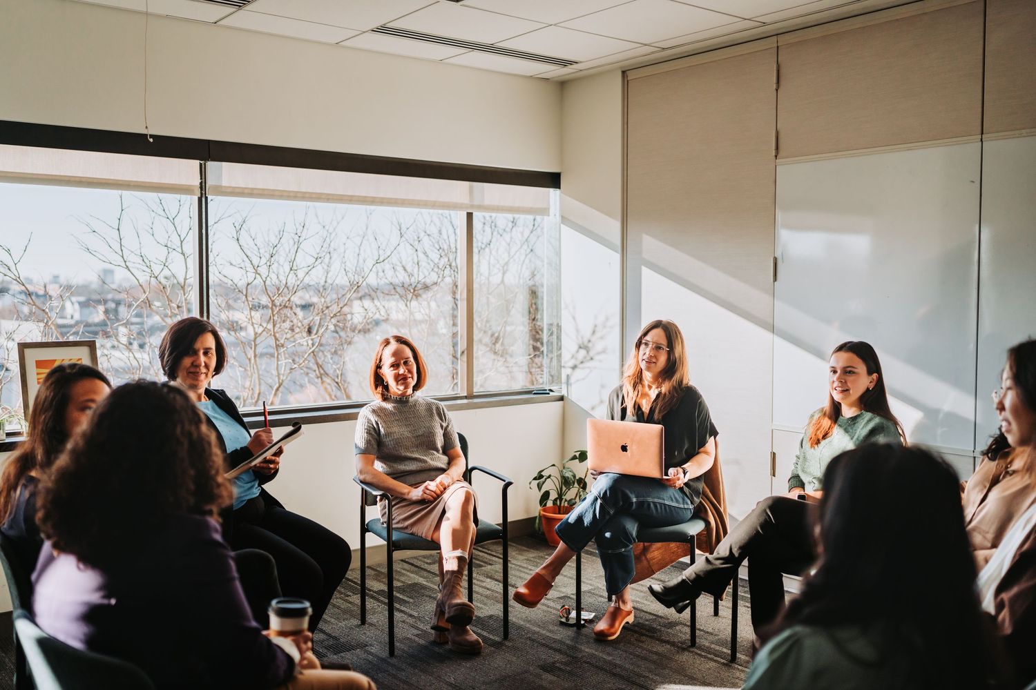 A group of people sit in chairs arranged in a circle during what appears to be a meeting or workshop session.