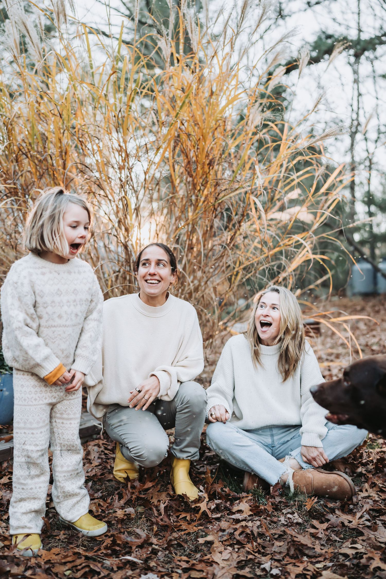 Group sitting on fallen leaves wearing cozy sweaters and laughing together outdoors.