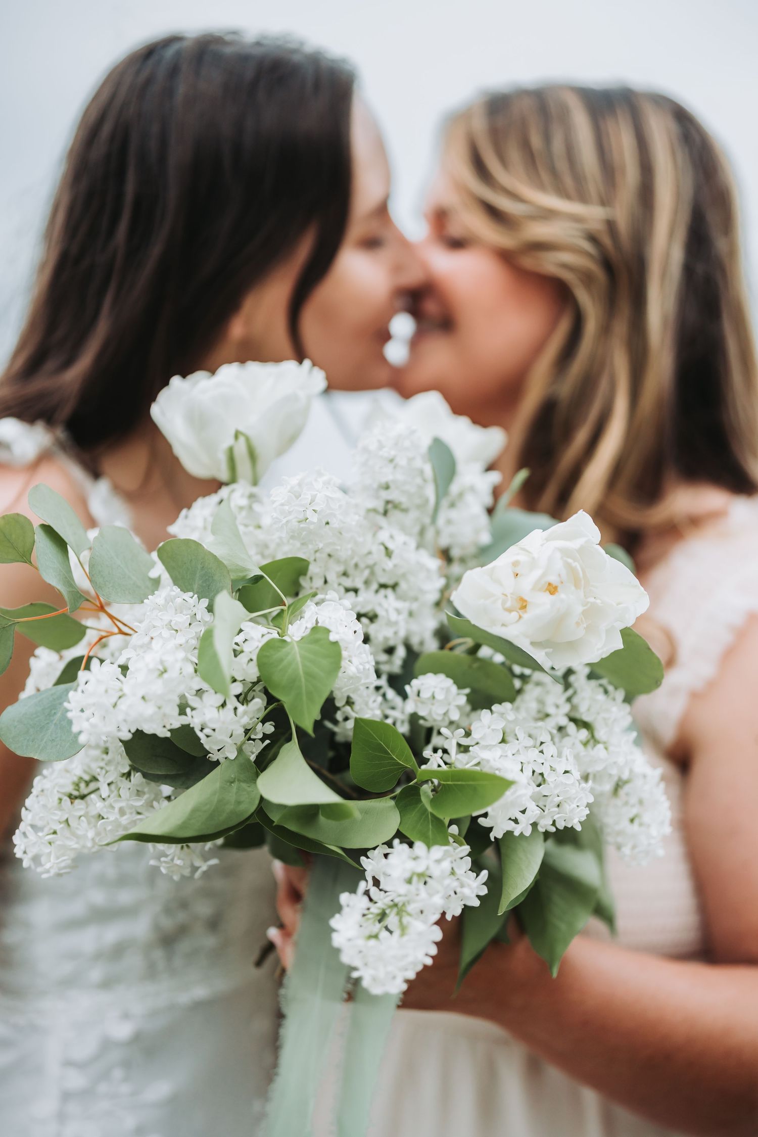 White lilacs and roses frame an intimate wedding moment against a soft, dreamy background.