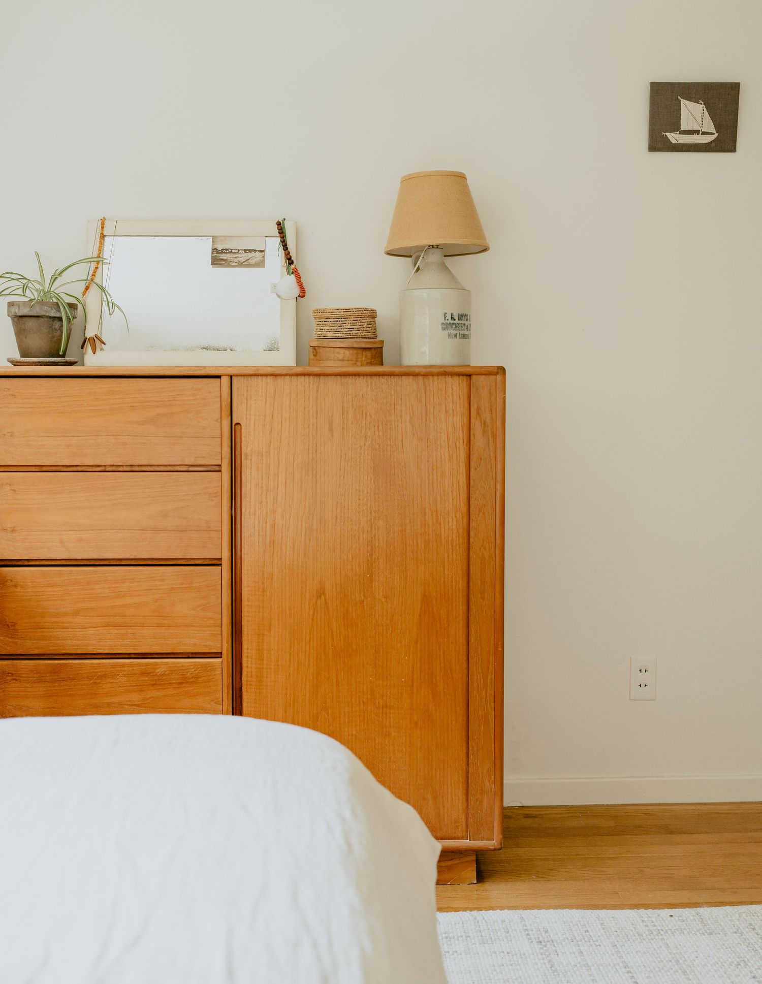 Minimalist bedroom corner with wooden dresser, white bedding, and vintage lamp creating a cozy aesthetic.