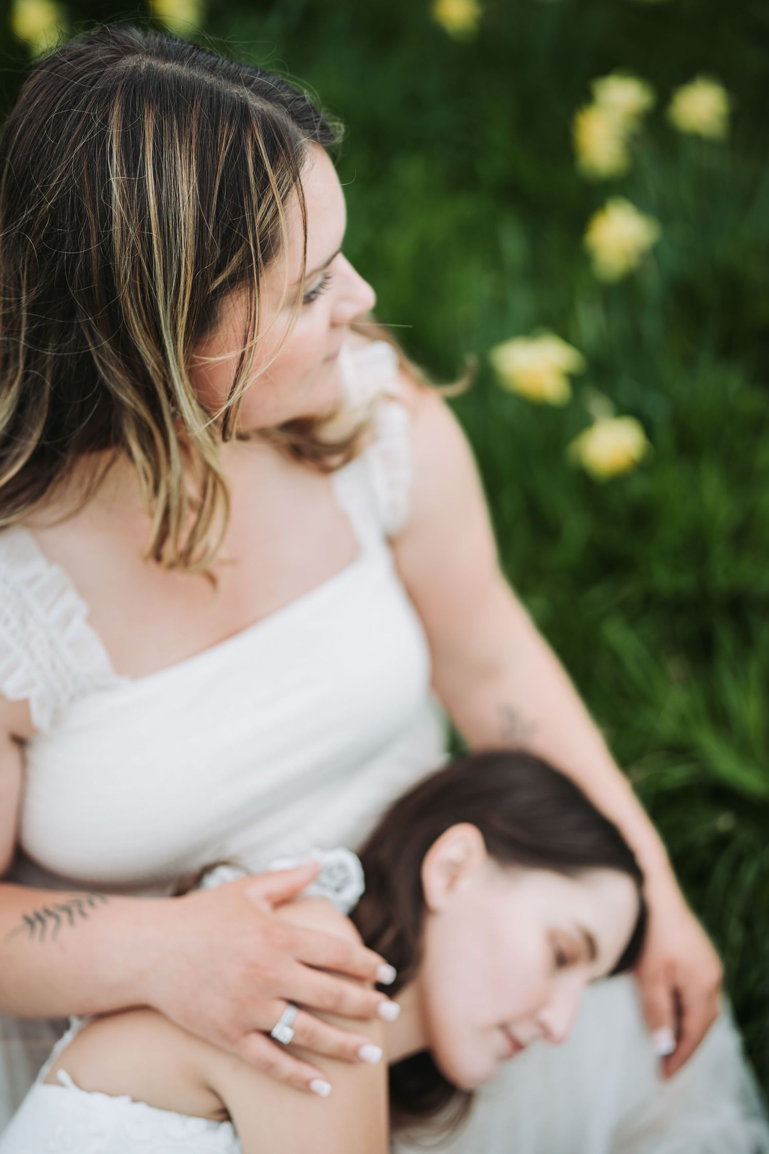 A romantic wedding couple embraces in a garden setting with yellow flowers and greenery in the background.