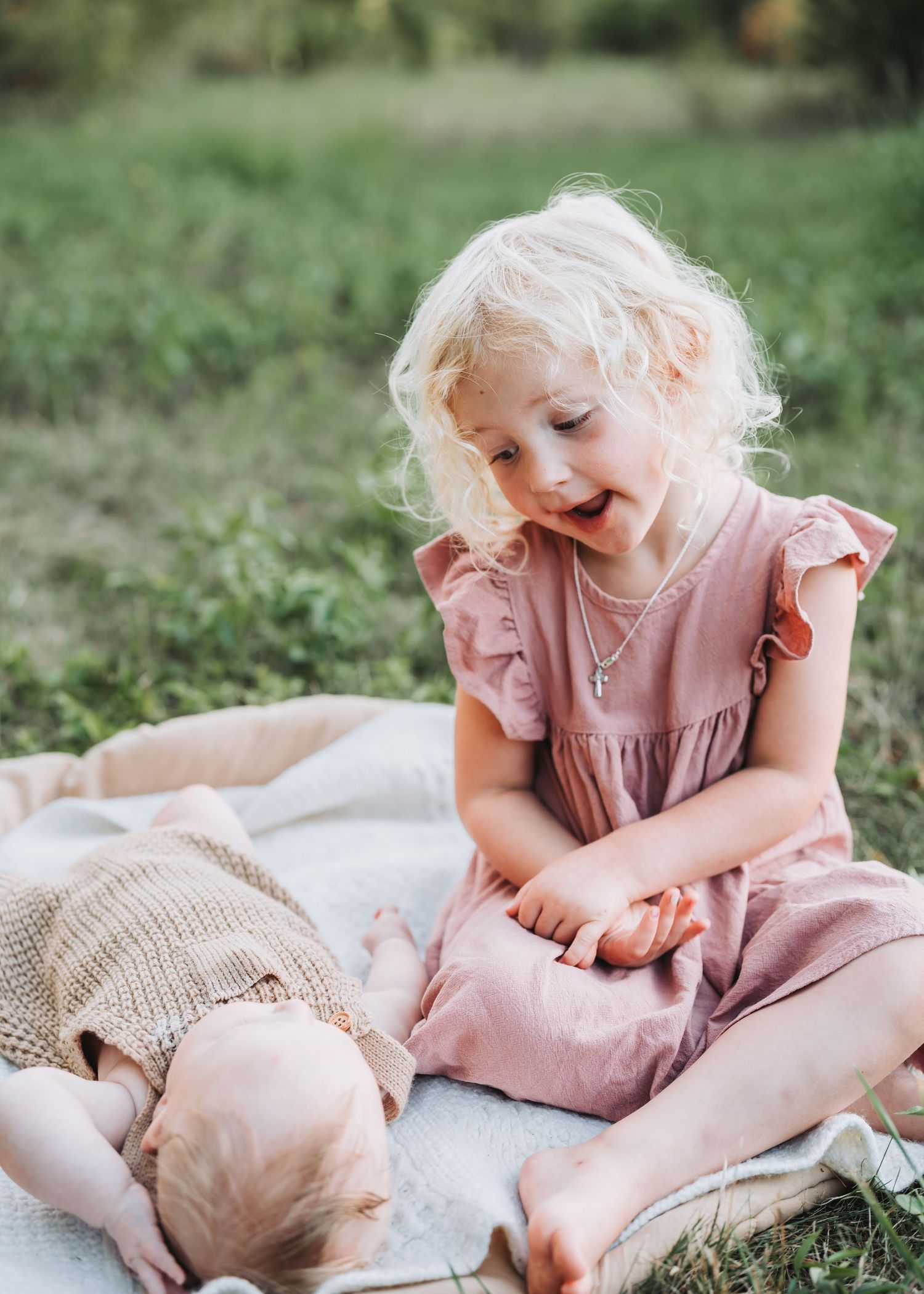 Sweet tender moments shared on a cozy blanket in the soft grass during a sunny outdoor photo session.