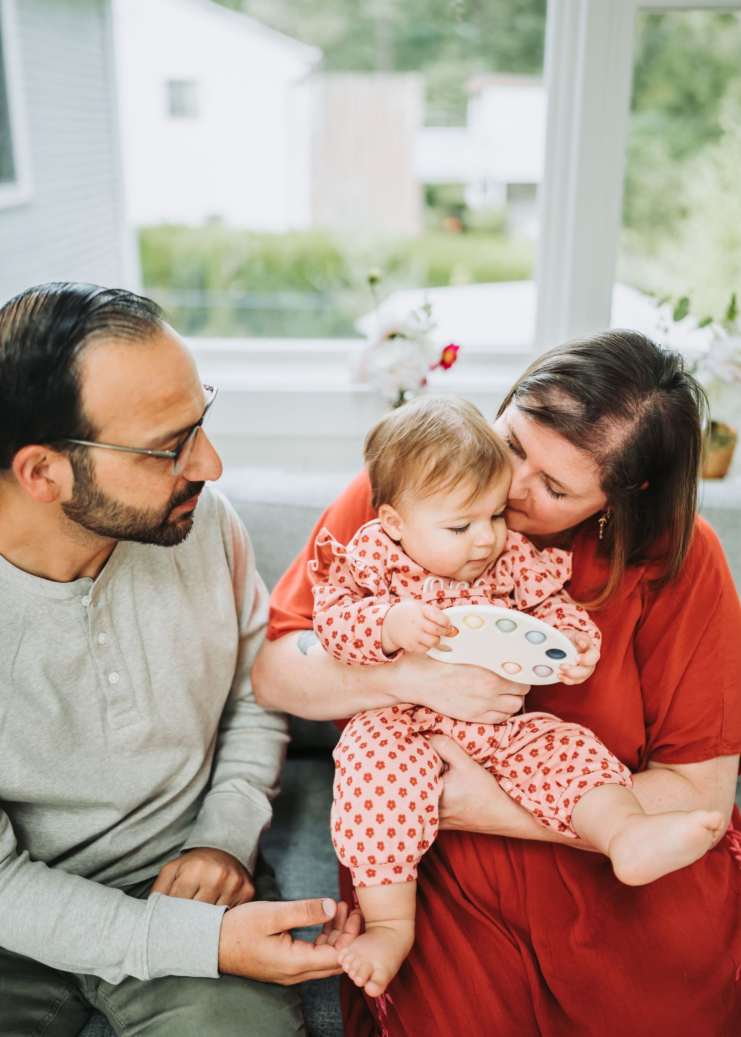 A family shares an intimate moment on a couch as they cuddle with a baby wearing a polka dot outfit.
